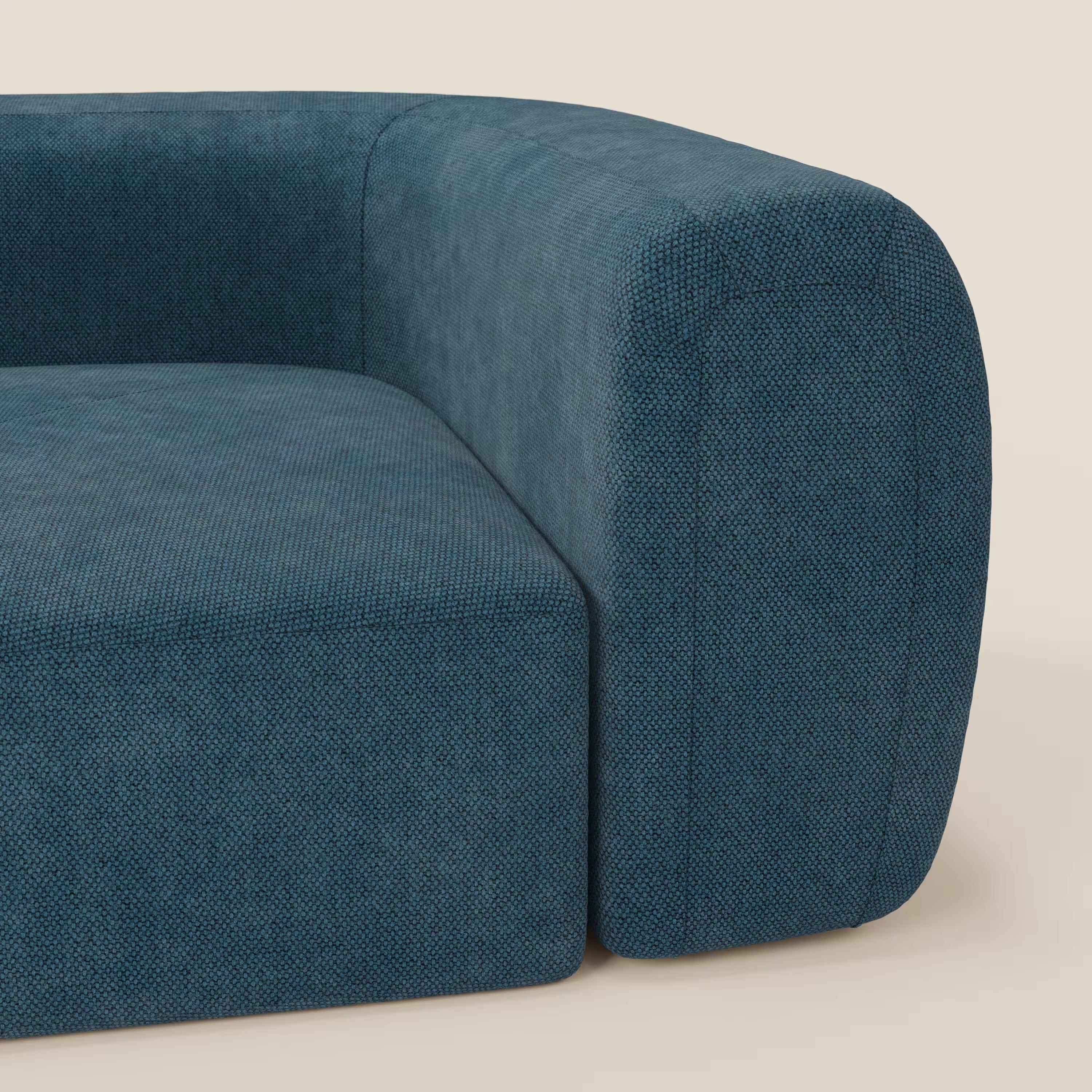 Un primo piano del BonBon Modulo angolare - Divano modulare componibile GF edition petrolio di Divani.Store mostra il suo rivestimento blu intenso, lo spesso bracciolo curvo e i bordi morbidi e arrotondati su uno sfondo beige semplice.