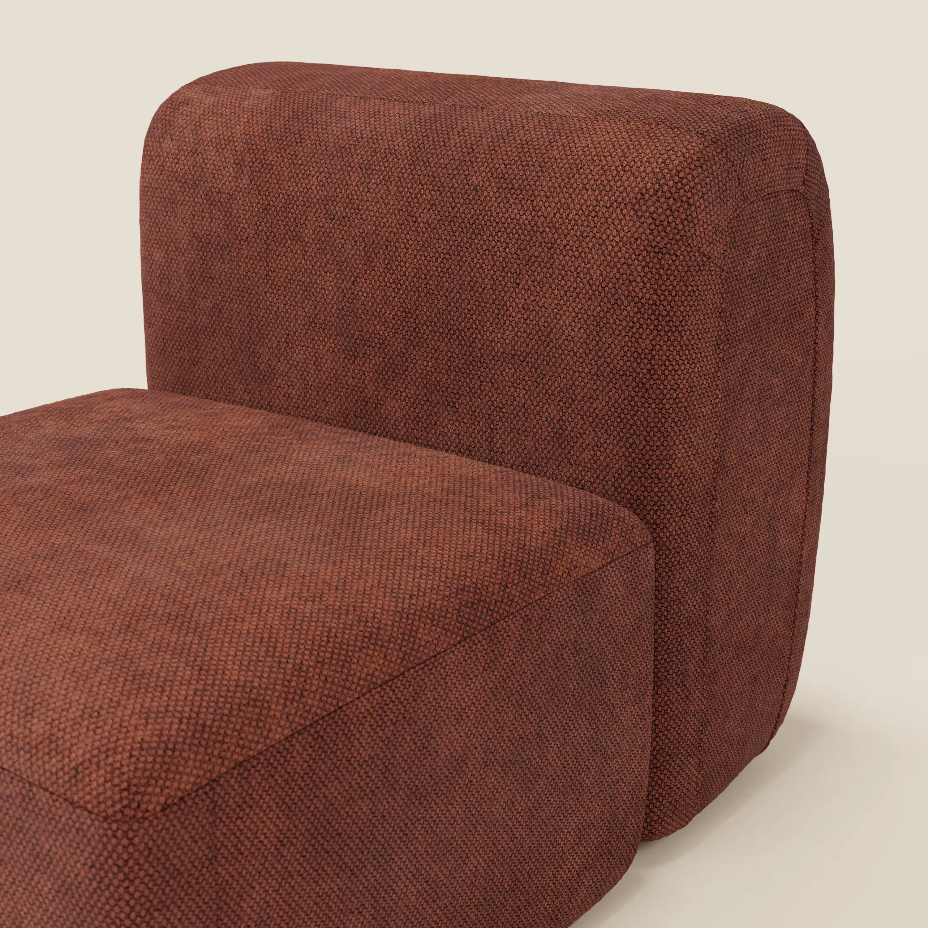 Primo piano del tappeto BonBon modulo centrale 70 cm - Grande Fratello edition di Divani.Store, una moderna seduta senza braccioli con cuscini spessi e arrotondati in tessuto testurizzato marrone rossiccio, su uno sfondo semplice bianco sporco.