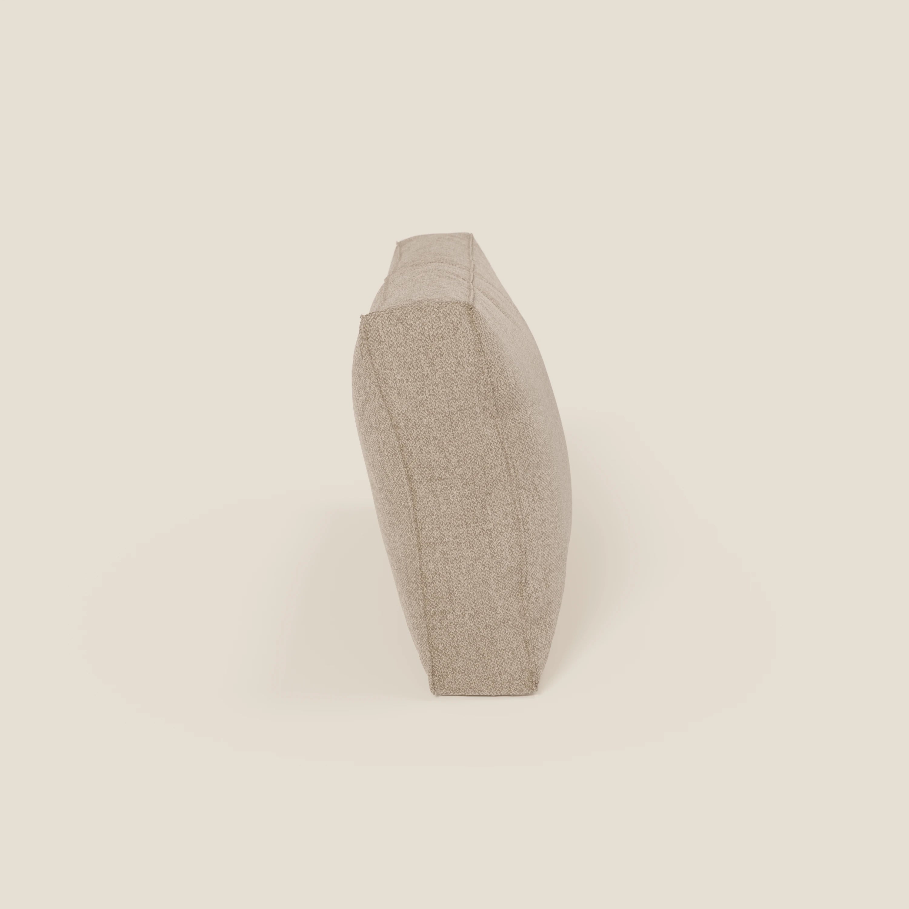 Un cuscino schienale BonBon di Divani.Store in smacchiabile T23 beige è mostrato in posizione verticale sul bordo stretto, visto di lato su uno sfondo beige chiaro. Il cuscino strutturato ha bordi leggermente arrotondati ed è disponibile in 2 misure.