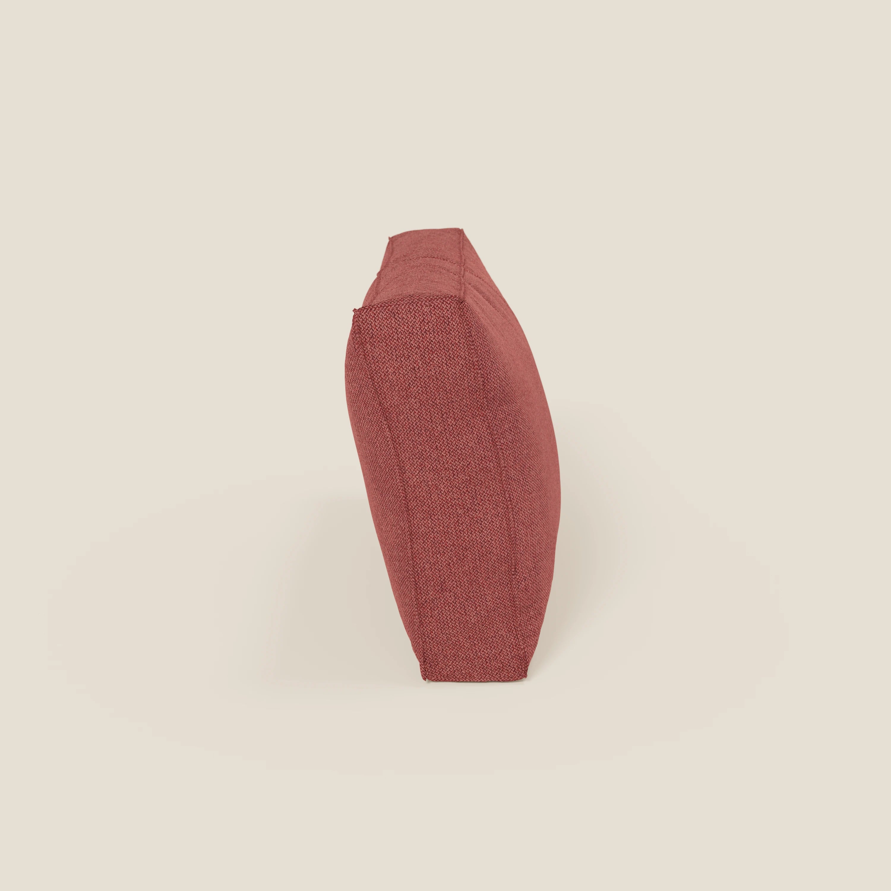 Il cuscino schienale BonBon di Divani.Store, in tessuto smacchiabile T23 rosso ciliegia, è presentato in posizione verticale sul bordo lungo su uno sfondo beige chiaro. La sua texture suggerisce morbidezza. Disponibile in 2 misure.