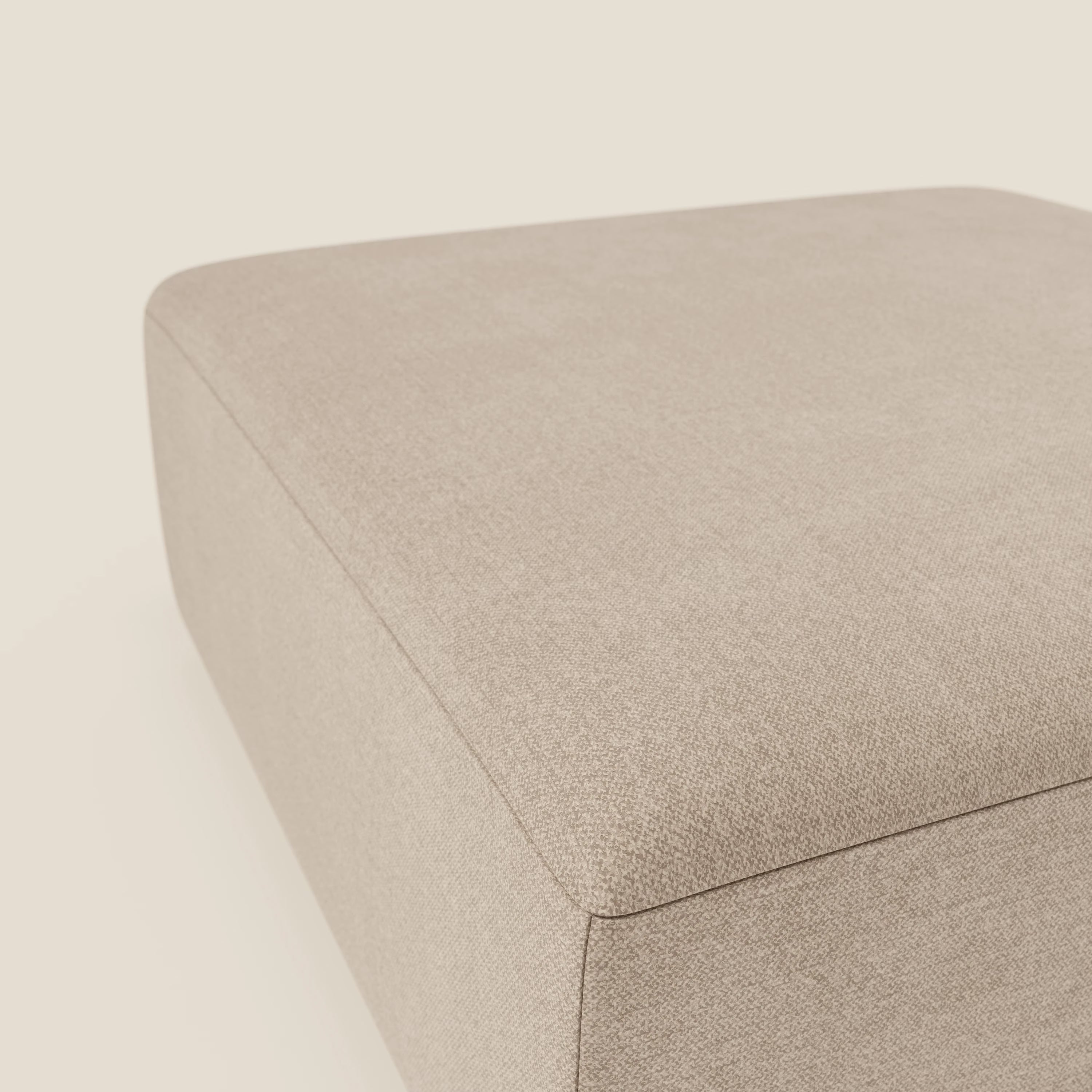 Primo piano del pouf divano modulare BonBon di Divani.Store in tessuto antimacchia T23 beige, caratterizzato da bordi lisci e arrotondati e da una trama di rivestimento visibile su uno sfondo bianco sporco.