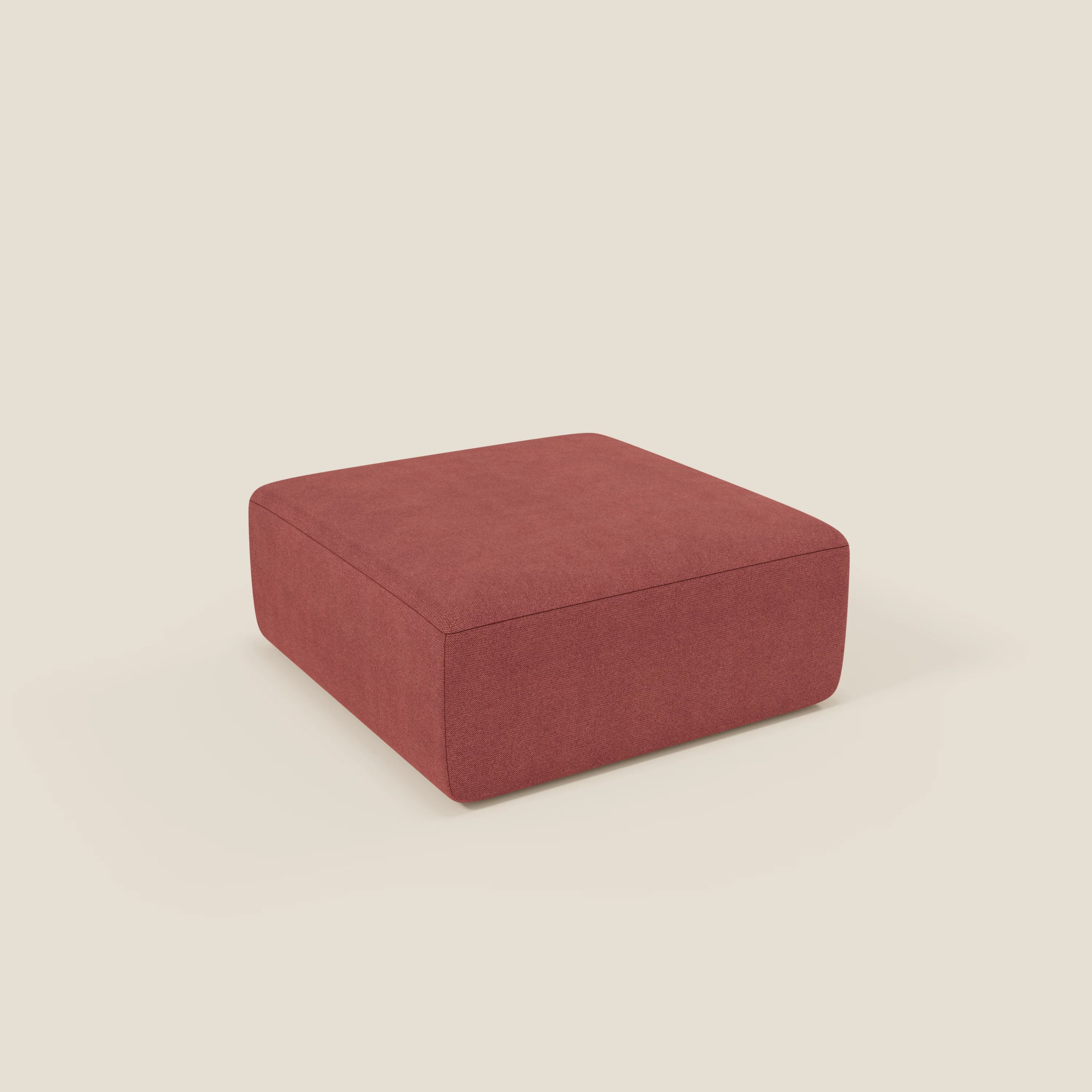 Il pouf divano modulare BonBon di Divani.Store, in tessuto T23 antimacchia rosso ciliegia, è caratterizzato da un'ampia forma quadrata con bordi arrotondati e un design minimalista, che poggia senza gambe su un fondo beige chiaro.