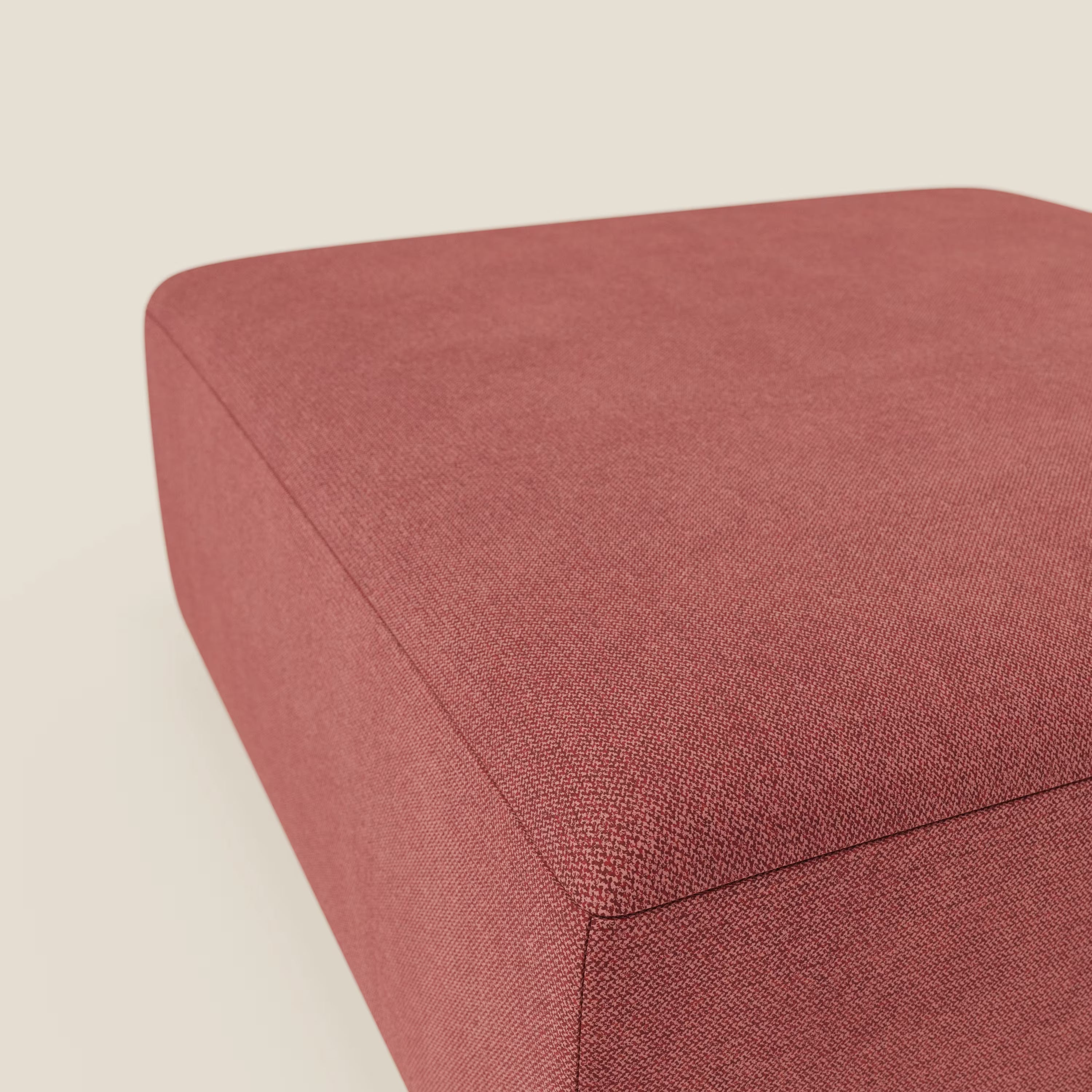 Primo piano del pouf divano modulare BonBon di Divani.Store in tessuto smacchiabile T23 rosso ciliegia, dalle linee pulite e dalla trama intrecciata, su uno sfondo beige chiaro che ne evidenzia la parte superiore e laterale.