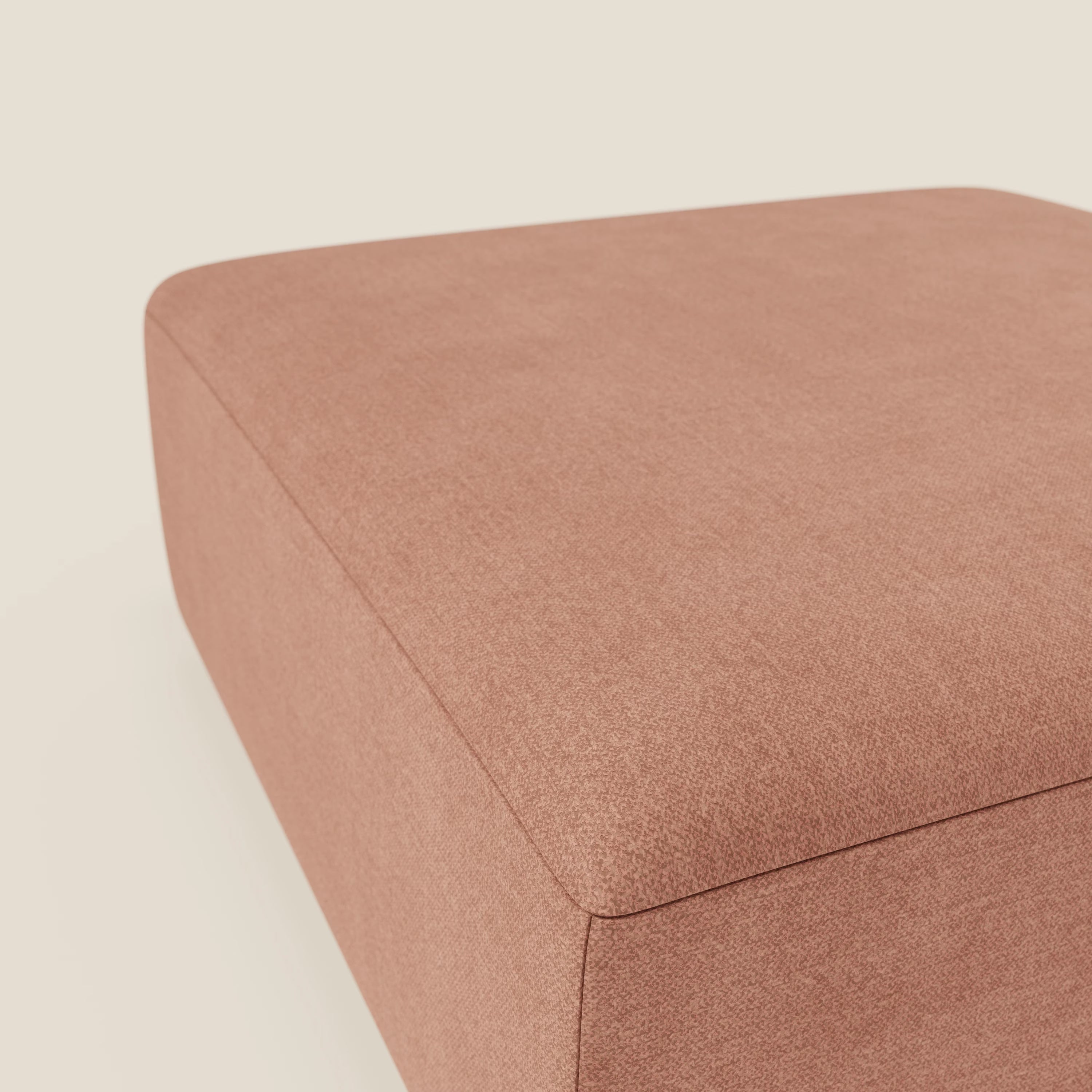 Primo piano del pouf divano modulare BonBon di Divani.Store, presentato in tessuto antimacchia T23 pesca. La forma quadrata e la superficie imbottita sottolineano le linee moderne e semplici su uno sfondo beige chiaro.