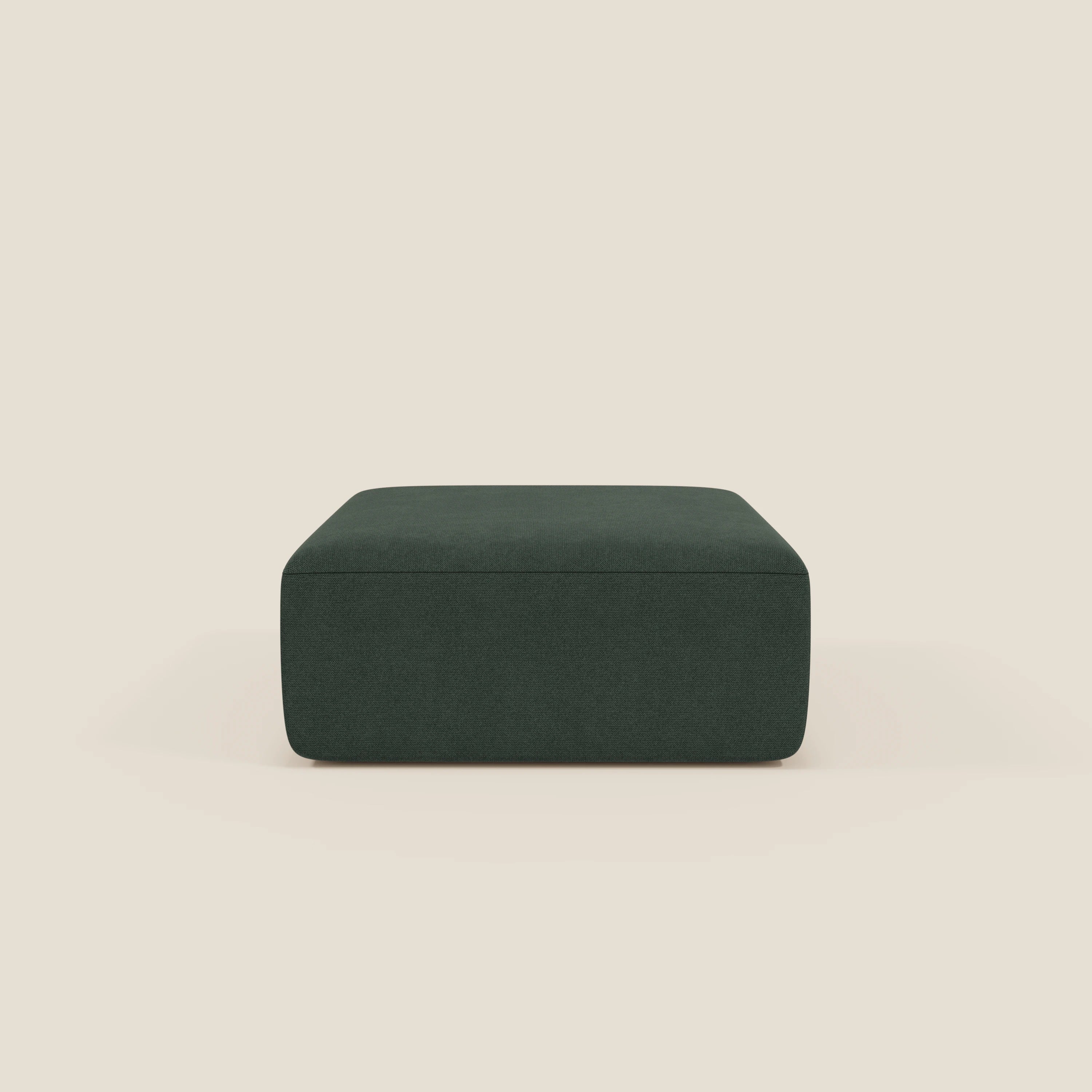 Il pouf divano modulare BonBon di Divani.Store, qui presentato in tessuto antimacchia T23 verde scuro, ha un design minimalista senza gambe con una morbida superficie imbottita e si trova al centro di uno sfondo beige chiaro.
