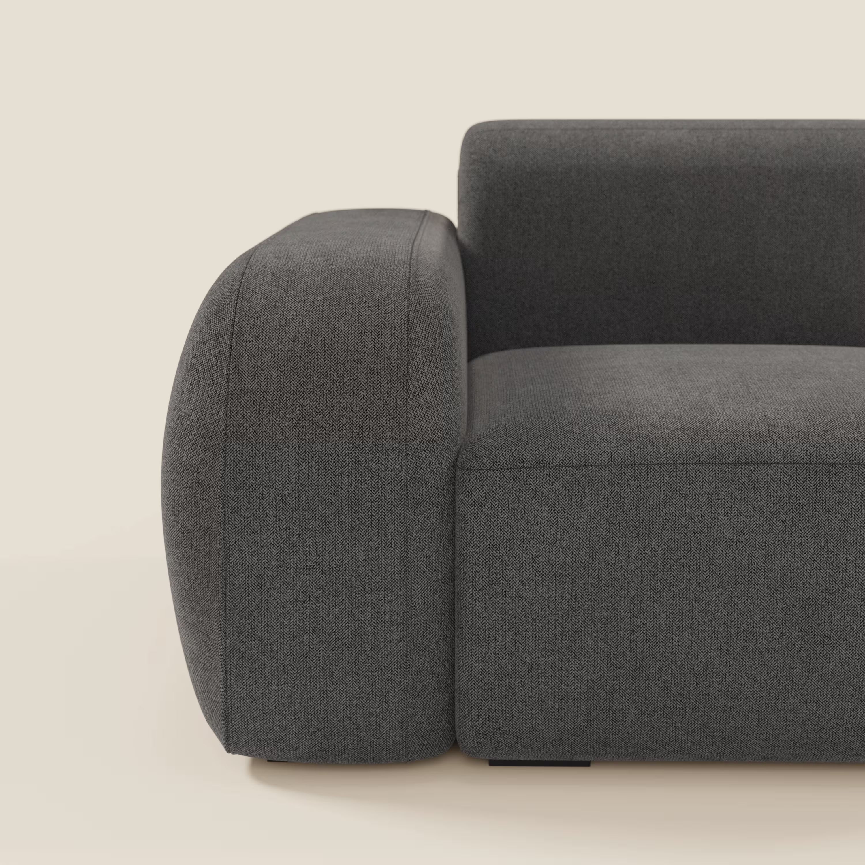 Un primo piano di Divani.Store BonBon modulo terminale 105 cm sinistro in tessuto smacchiabile T23 antracite mostra braccioli spessi e arrotondati e linee minimaliste, con il bracciolo sinistro e la seduta su uno sfondo beige chiaro.