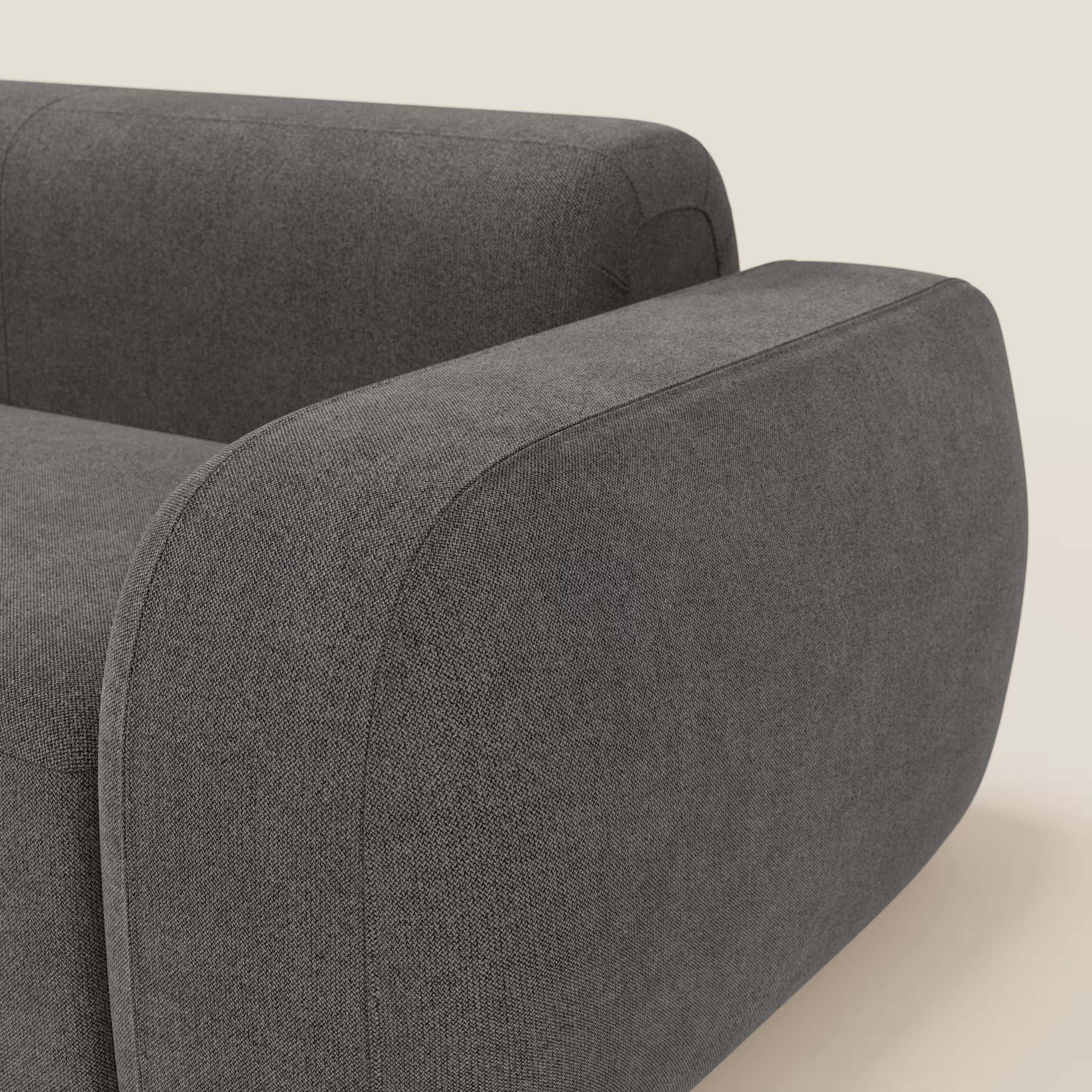 Un primo piano del BonBon Divano modulare Lineare 220 di Divani.Store mostra il bracciolo arrotondato e morbido in tessuto smacchiabile T23 antracite, con bordi lisci e texture visibile, su uno sfondo beige chiaro per un look moderno.