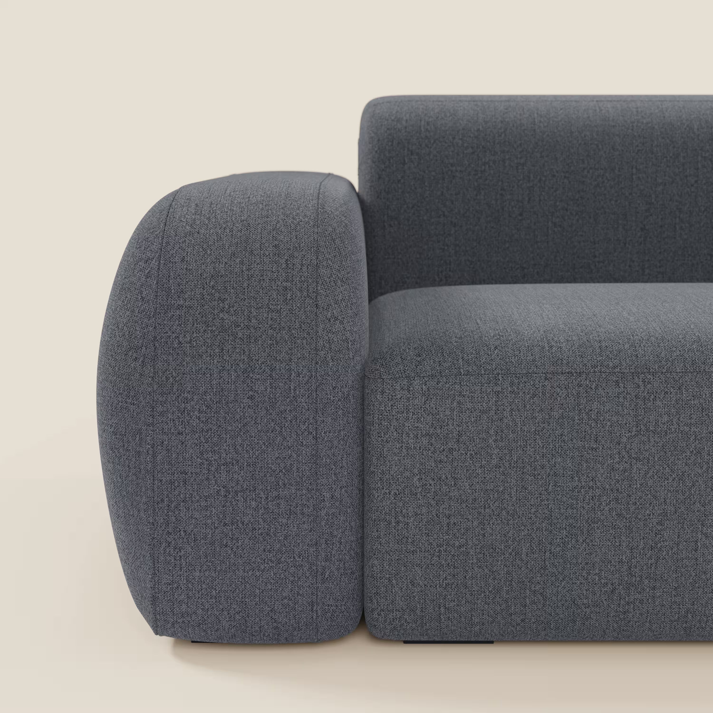 Un primo piano del BonBon Divano modulare Lineare 220 di Divani.Store presenta il bracciolo sinistro e la seduta unica in tessuto grafite blu T23 smacchiabile, morbido e arrotondato, su uno sfondo chiaro.