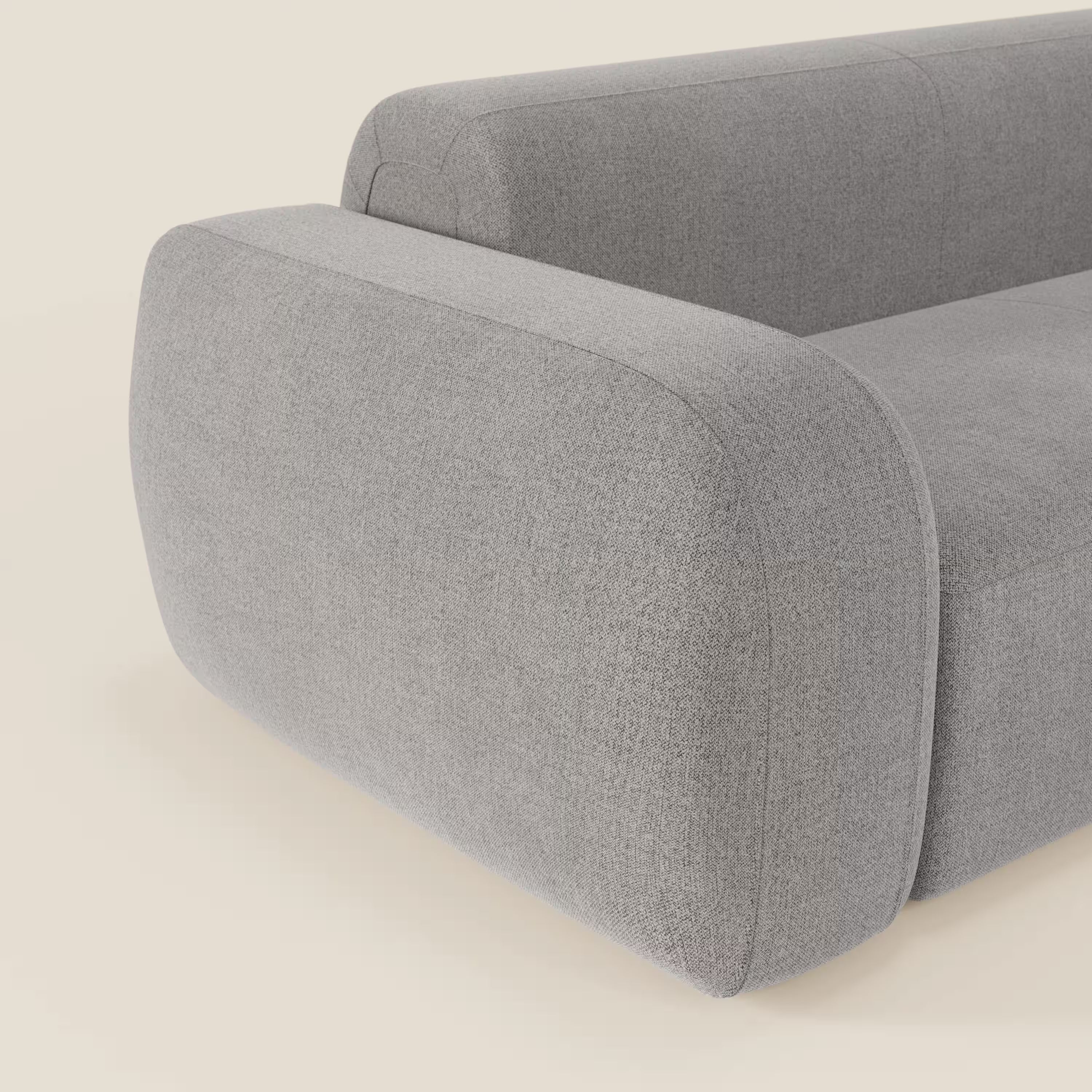 Un primo piano del BonBon Divano modulare Lineare 220 di Divani.Store mostra il bracciolo e lo schienale liscio e arrotondato in tessuto antimacchia T23 grigio chiaro, che mette in risalto il design minimalista su uno sfondo bianco sporco.