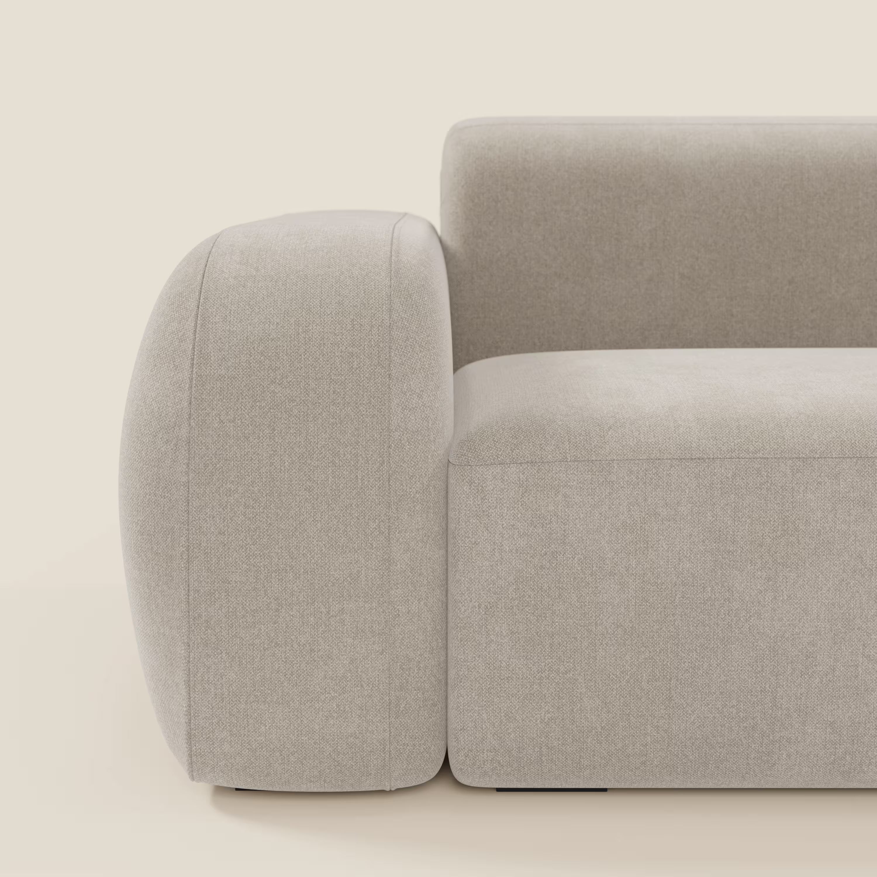 Un primo piano del BonBon Divano modulare Lineare 220 di Divani.Store in tessuto smacchiabile T23 panna mostra il bracciolo sinistro, la seduta e lo schienale, caratterizzati da un design contemporaneo con linee morbide e arrotondate su uno sfondo chiaro.