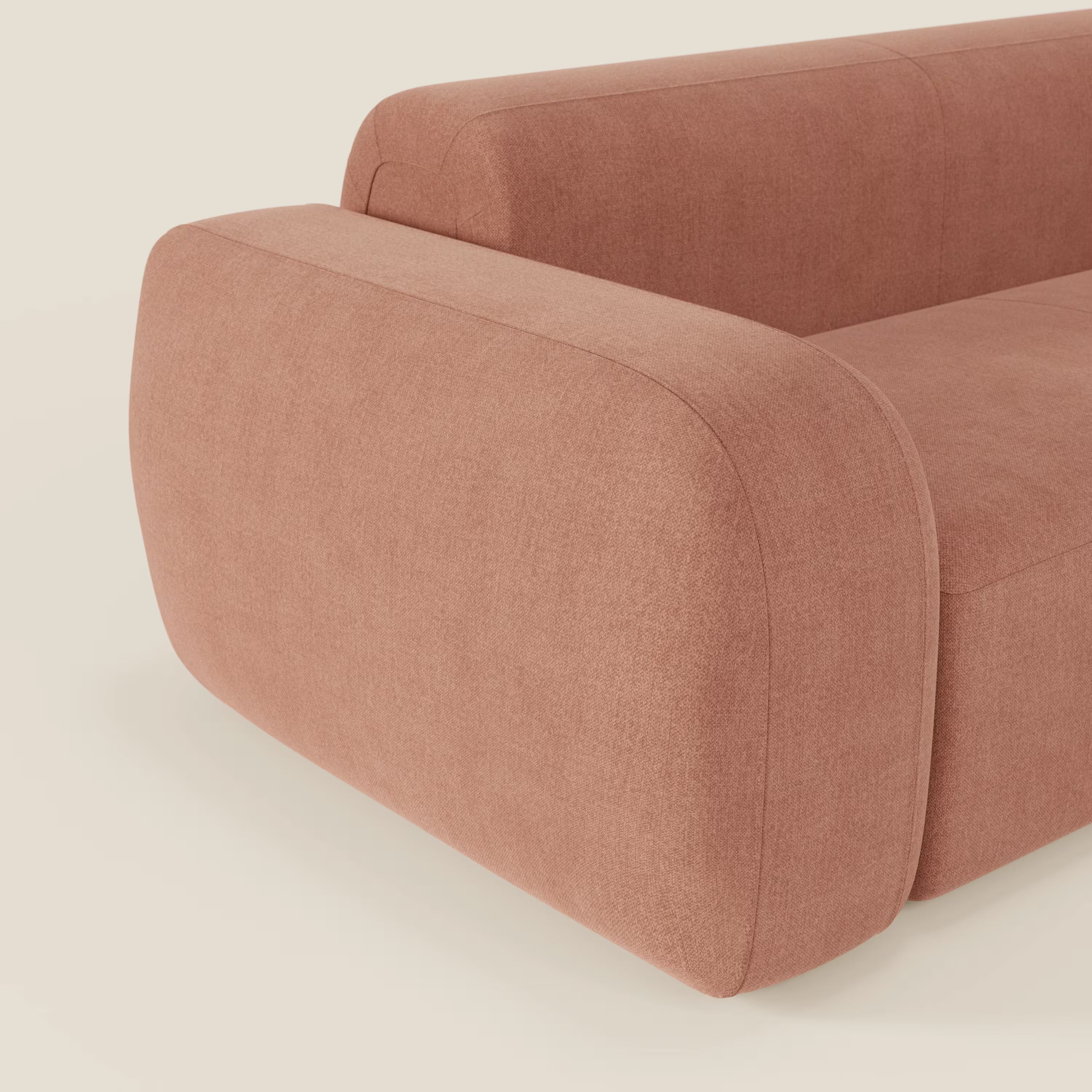 Un primo piano del BonBon Divano modulare Lineare 220 di Divani.Store è caratterizzato da braccioli e schienale arrotondati e sovradimensionati in tessuto smacchiabile T23 pesca, su uno sfondo bianco chiaro.