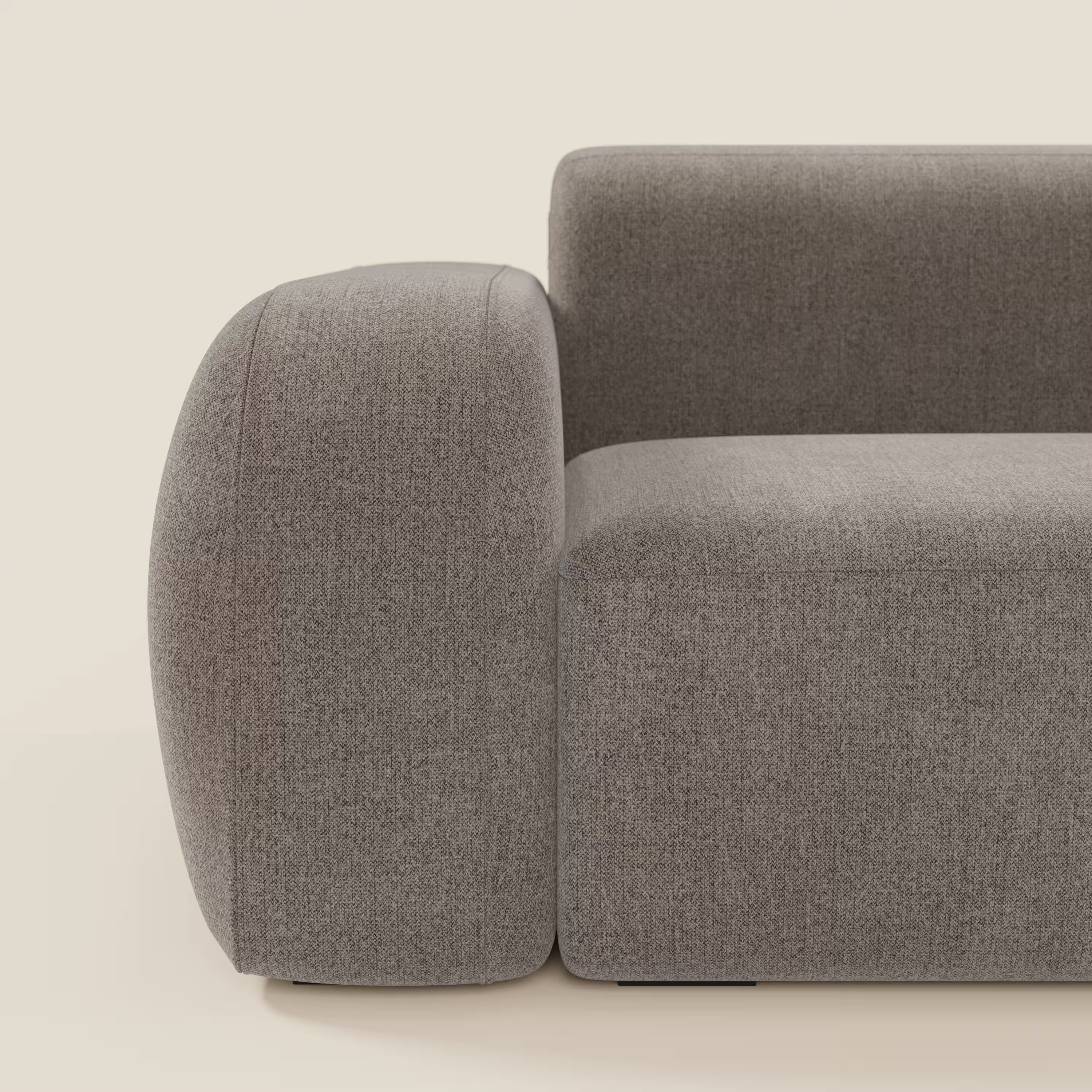 Un primo piano del BonBon Divano modulare Lineare 220 di Divani.Store mostra i braccioli spessi e arrotondati e la seduta singola in tessuto antimacchia T23 talpa. L'aspetto morbido e minimale e le linee pulite risaltano su uno sfondo chiaro; viene mostrato solo il lato sinistro.