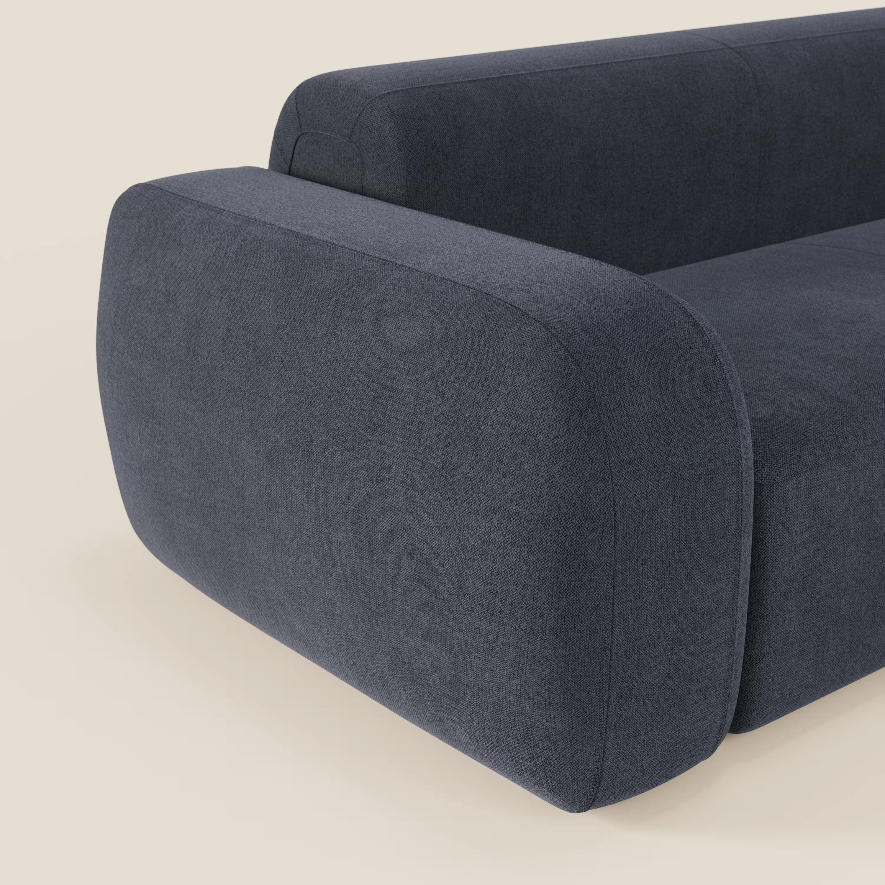 Primo piano del divano componibile BonBon Divano di Divani.Store in tessuto smacchiabile T23 blu ardesia, caratterizzato da ampi braccioli arrotondati e da una morbida imbottitura su uno sfondo beige che ne evidenzia le linee pulite e minimaliste.