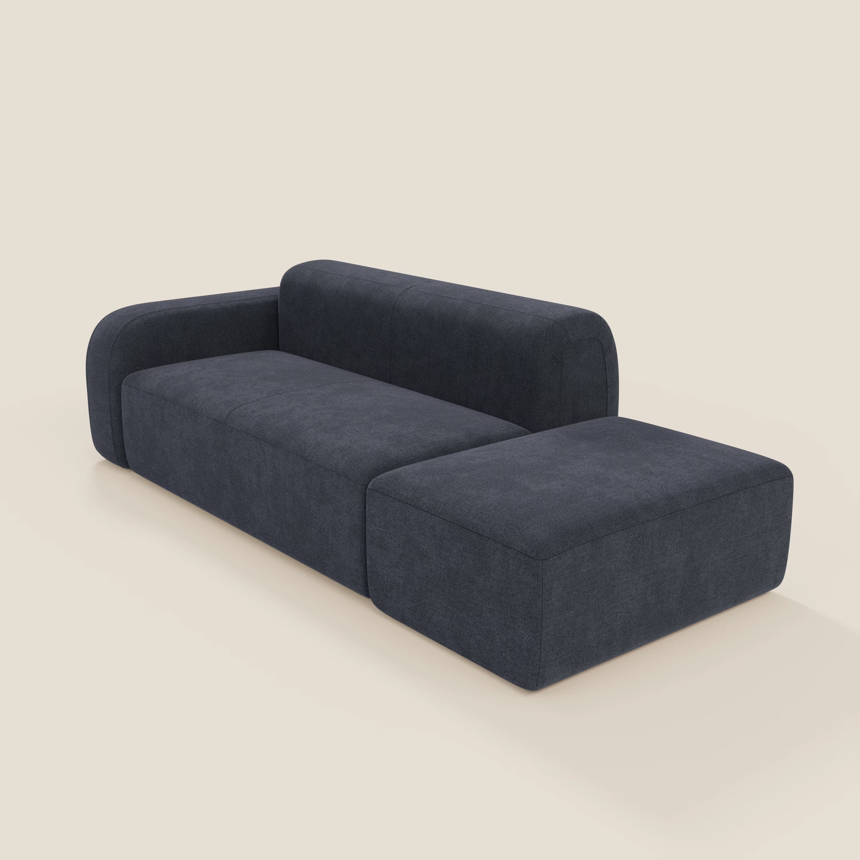 Il BonBon Divano componibile di Divani.Store in smacchiabile T23 blu ardesia è caratterizzato da linee pulite, schienale basso, ampio bracciolo sinistro, chaise lounge destra e versatile pouf terminale, presentato su uno sfondo bianco sporco.