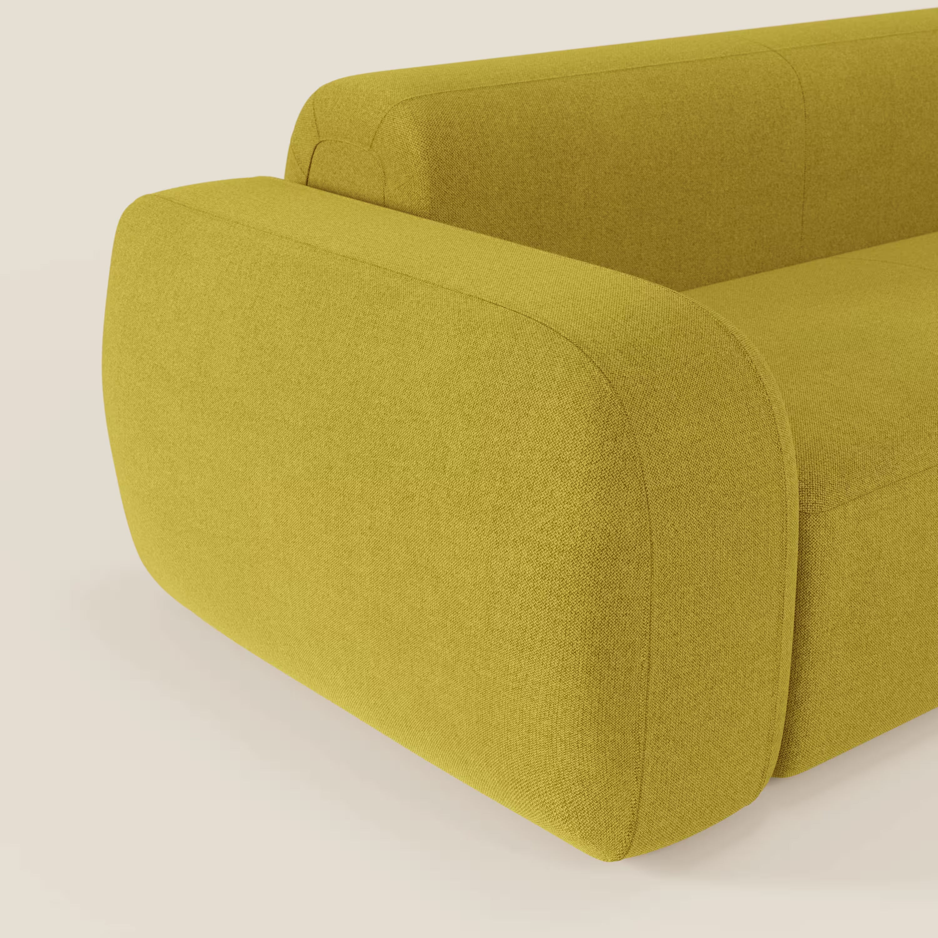 Un primo piano del BonBon Divano componibile di Divani.Store in smacchiabile T23 giallo sole mostra i braccioli arrotondati e imbottiti e i bordi curvi. Il tessuto strutturato e lo sfondo neutro mettono in risalto la vivace tonalità di giallo del divano.