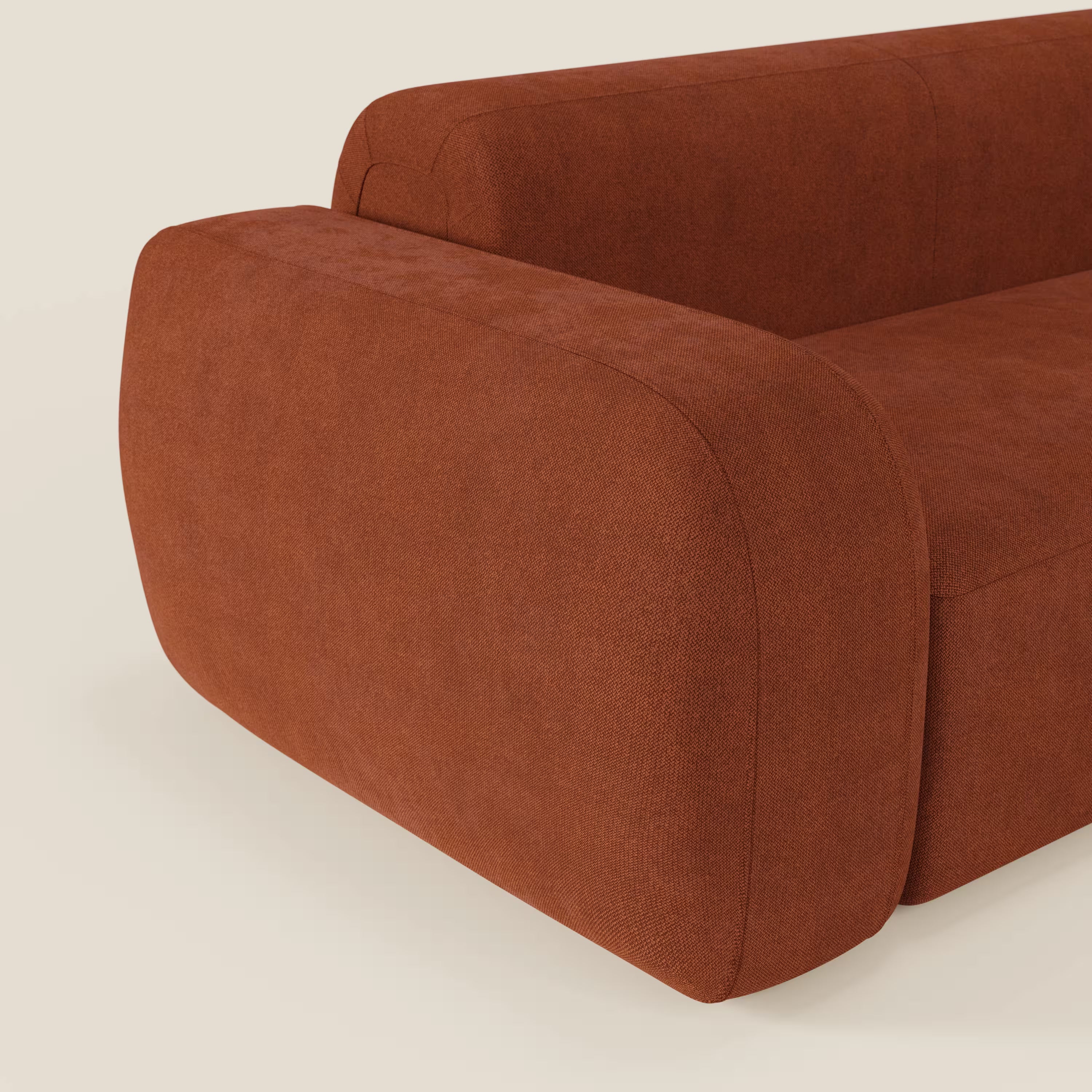 Primo piano del BonBon Divano componibile di Divani.Store in tessuto smacchiabile T23 ruggine, caratterizzato da un ampio bracciolo arrotondato, parte dello schienale e un pouf terminale dalle curve morbide su uno sfondo bianco sporco.