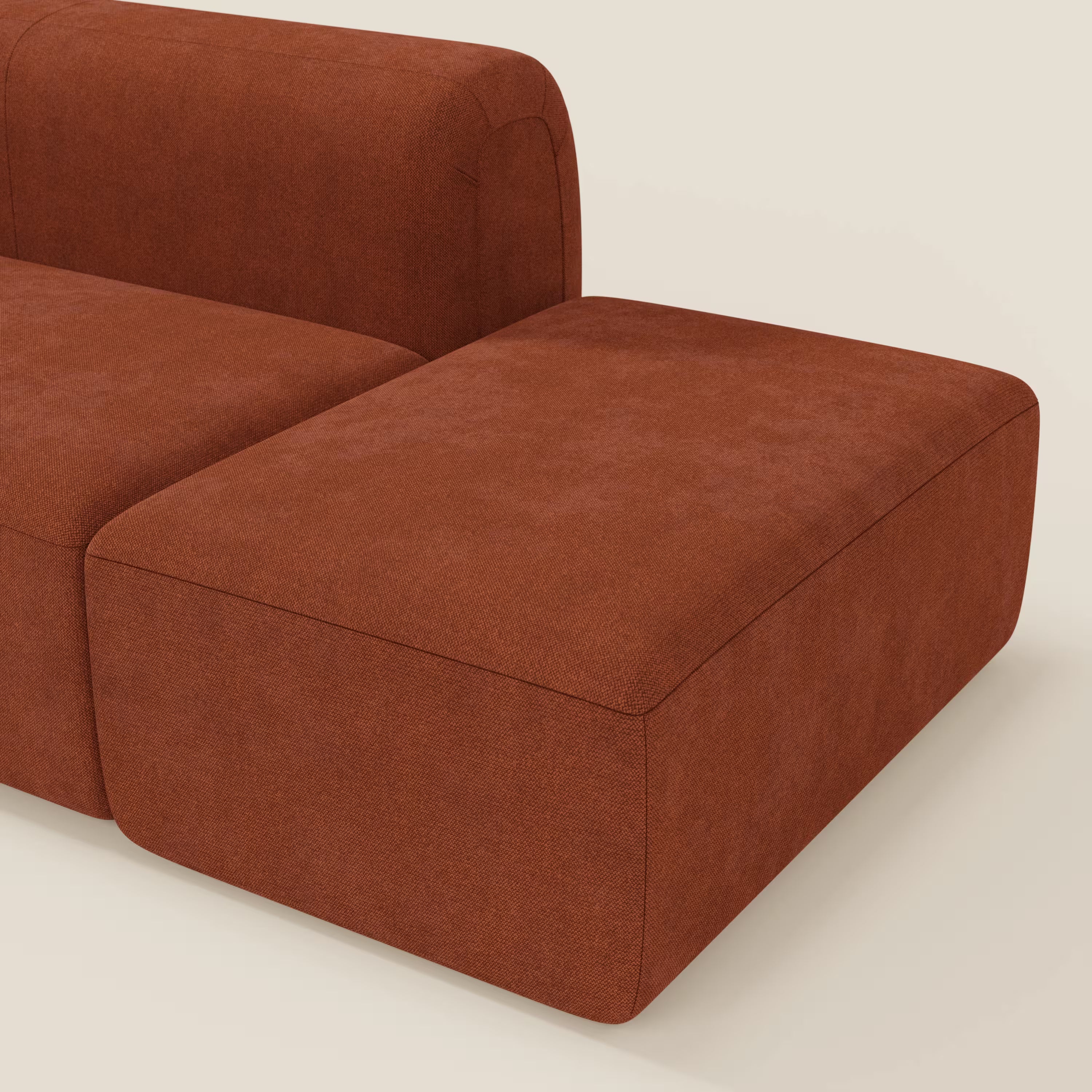 Il divano modulare componibile BonBon di Divani.Store, qui presentato in tessuto antimacchia T23 ruggine con pouf terminale, è caratterizzato da linee pulite e profilo basso su uno sfondo beige chiaro.