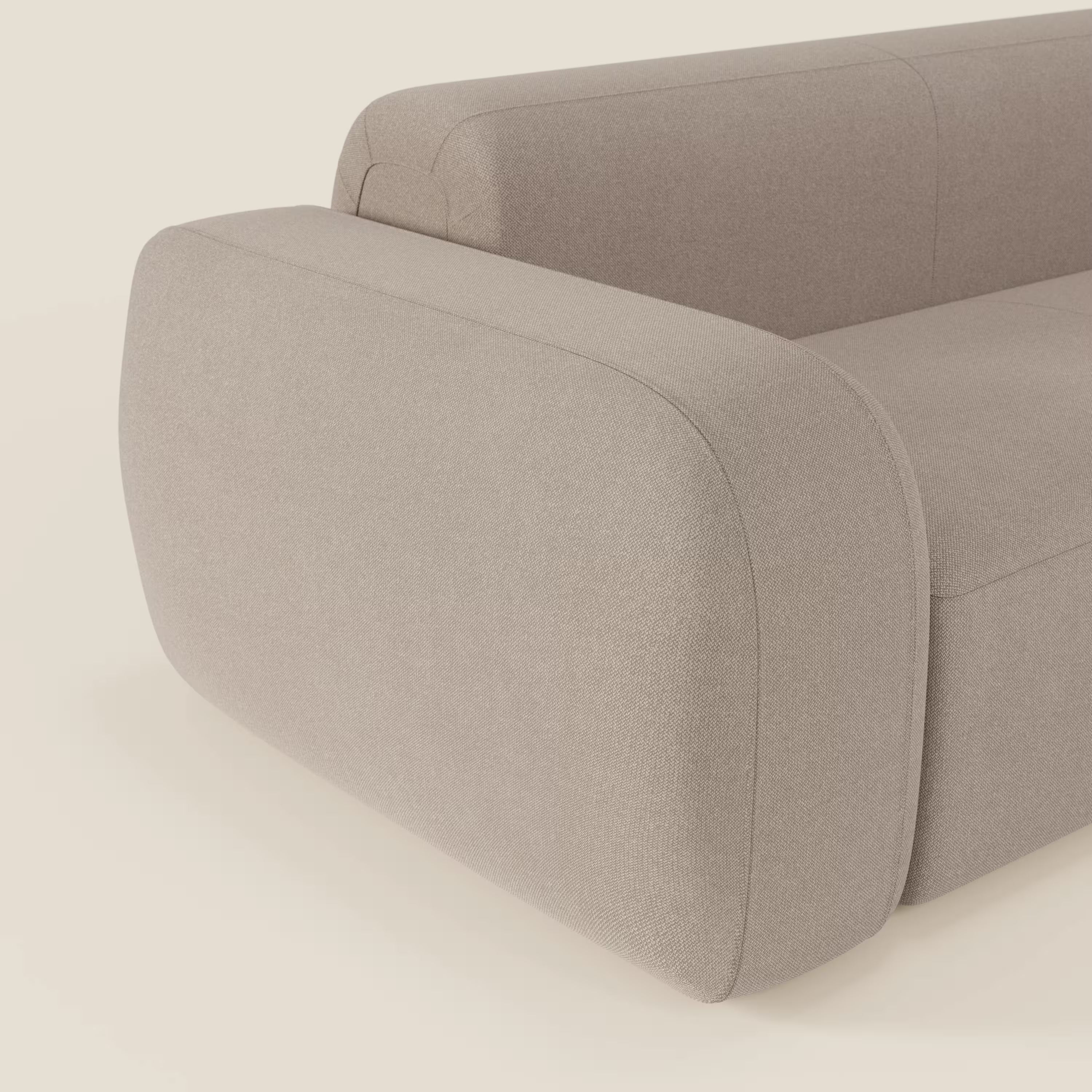 Un primo piano di BonBon Divano componibile di Divani.Store in smacchiabile T23 tortora mostra i braccioli e lo schienale arrotondati, il rivestimento liscio e testurizzato e lo sfondo neutro che ne evidenzia il design minimalista.