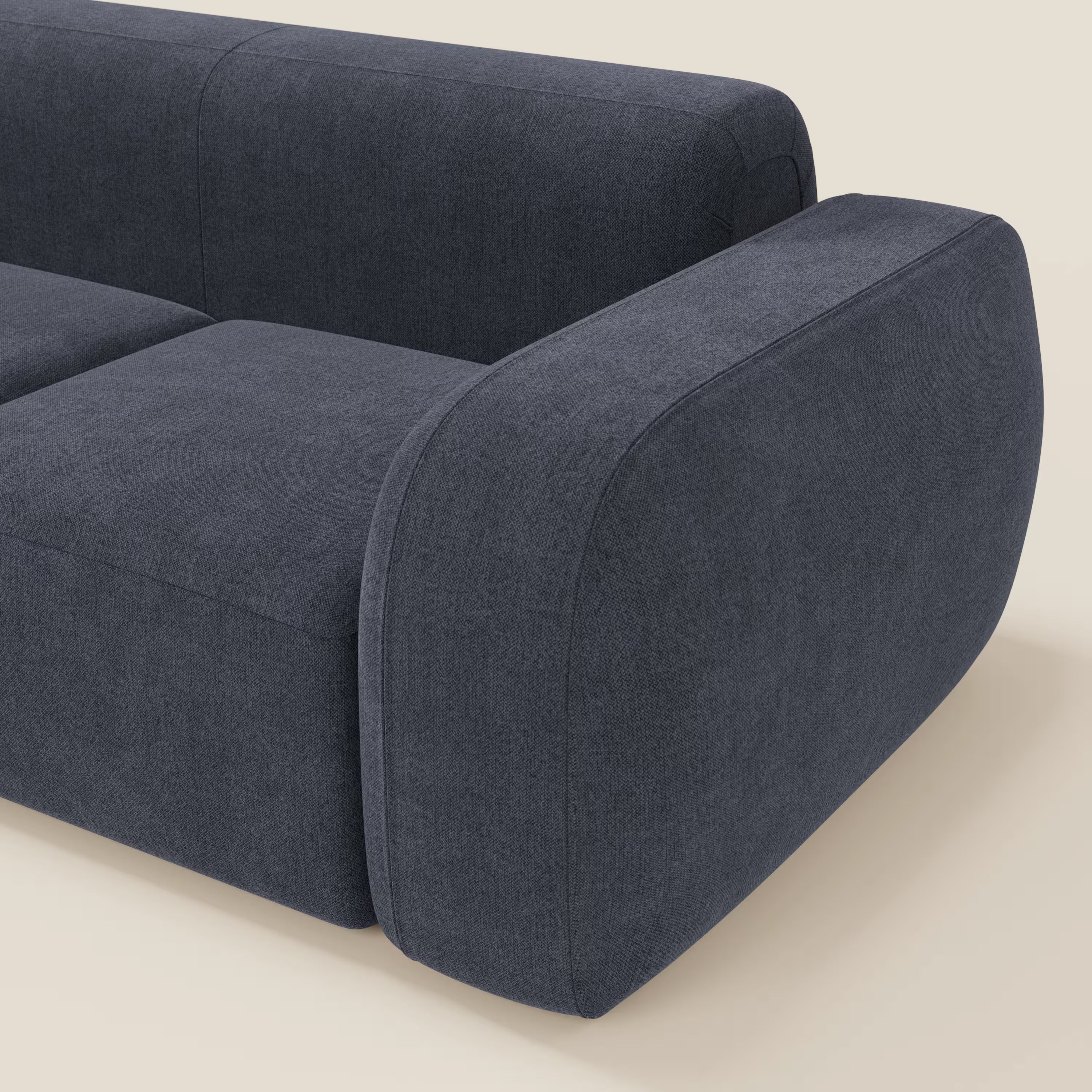 Primo piano del BonBon Divano modulare componibile - Composizione Spaccamattone di Divani.Store in smacchiabile T23 blu ardesia, che mostra le sue moderne linee arrotondate con parte della seduta, dello schienale e un bracciolo su uno sfondo beige chiaro.