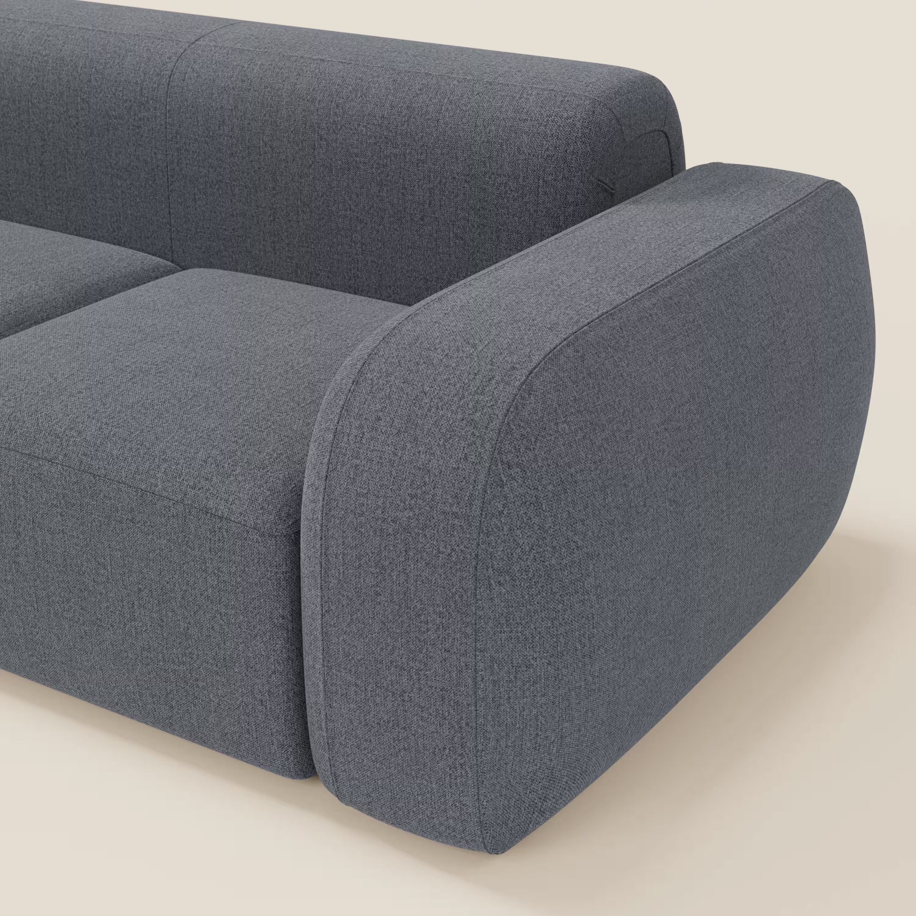 Un primo piano del BonBon Divano modulare componibile - Composizione Spaccamattone di Divani.Store in smacchiabile T23 blu grafite, che evidenzia il bracciolo, lo schienale e la seduta arrotondati su uno sfondo beige chiaro.