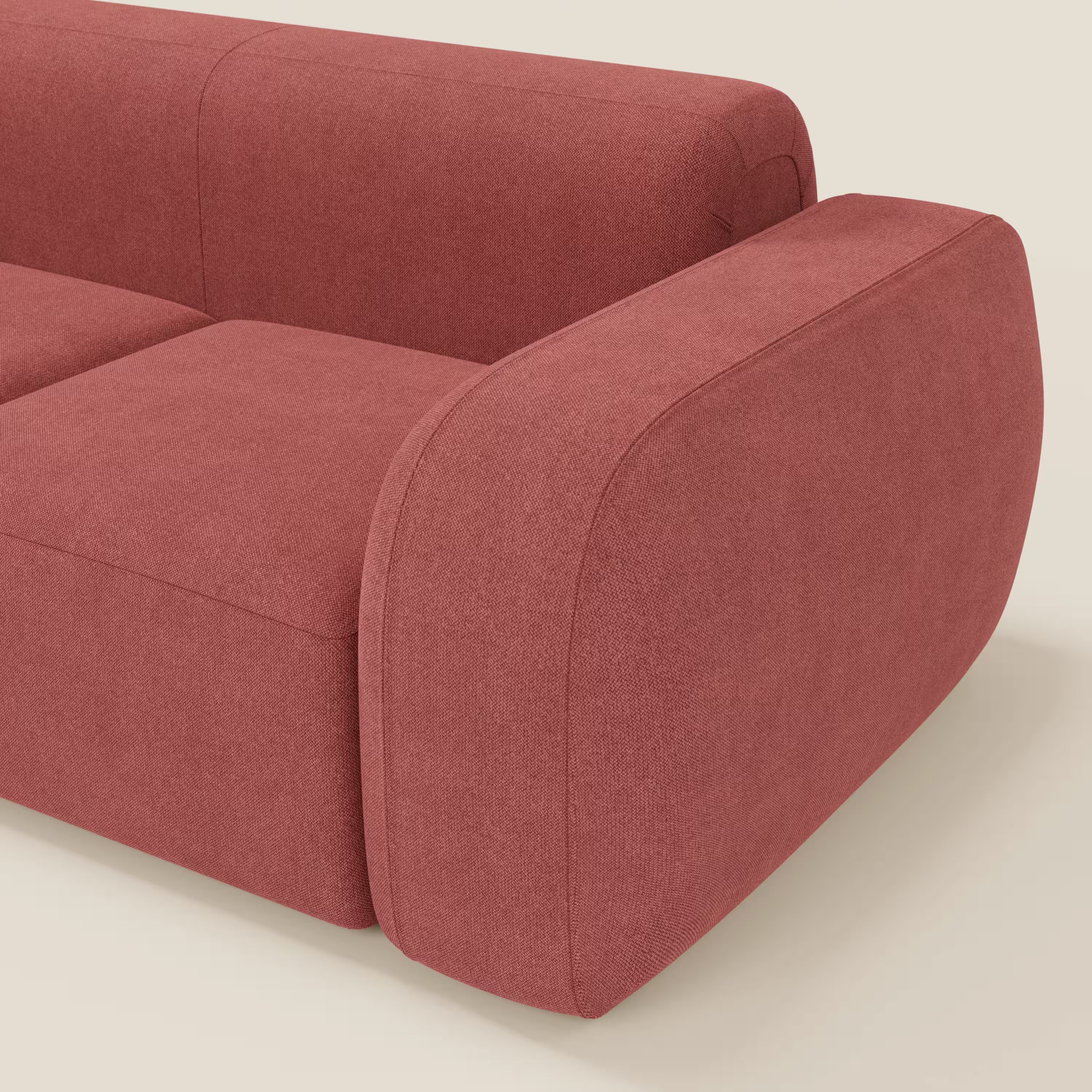 Un primo piano del BonBon Divano modulare componibile - Composizione Spaccamattone di Divani.Store mostra il tessuto lavabile T23 rosso ciliegia, il bracciolo sinistro e i due cuscini di seduta, sottolineando il suo design unico e minimalista. Lo sfondo è bianco sporco.