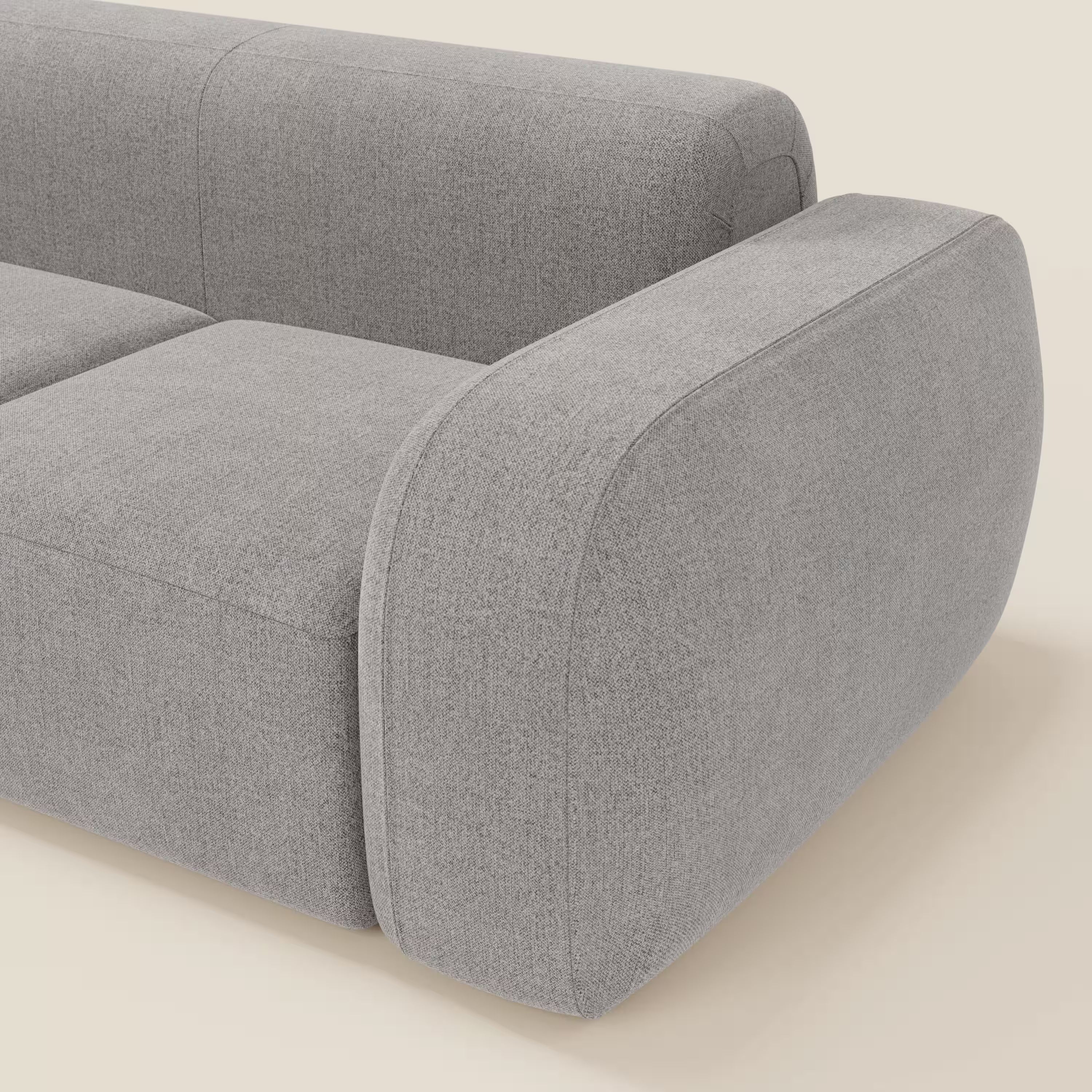 Un primo piano del BonBon Divano modulare componibile - Composizione Spaccamattone di Divani.Store in smacchiabile T23 grigio mostra un bracciolo e cuscini di seduta con bordi lisci e arrotondati e un design minimalista su uno sfondo chiaro.