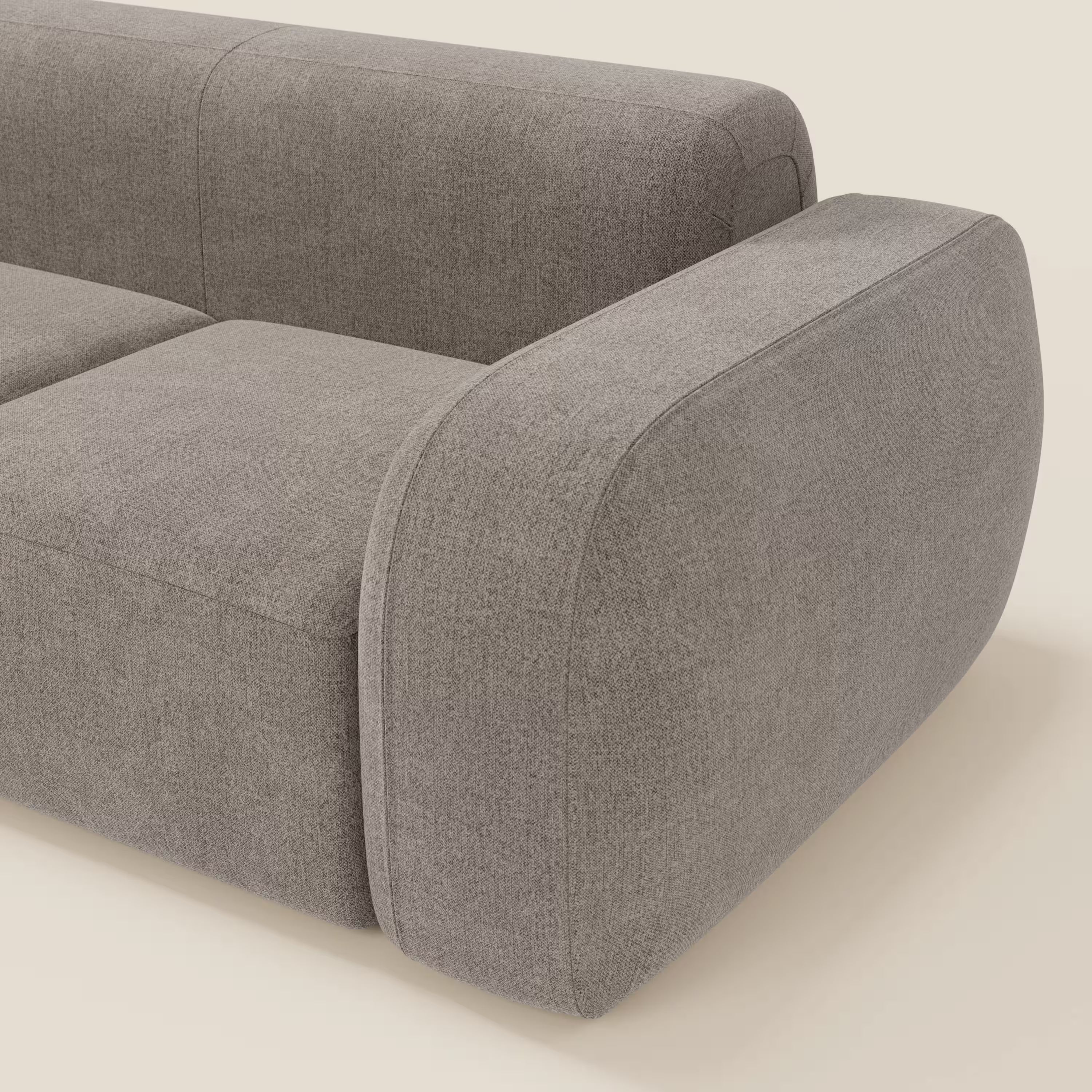 Un primo piano del BonBon Divano componibile - Composizione Spaccamattone di Divani.Store in tessuto smacchiabile T23 talpa, che mette in evidenza il bracciolo e lo schienale arrotondati su uno sfondo beige chiaro per uno stile moderno e minimalista.