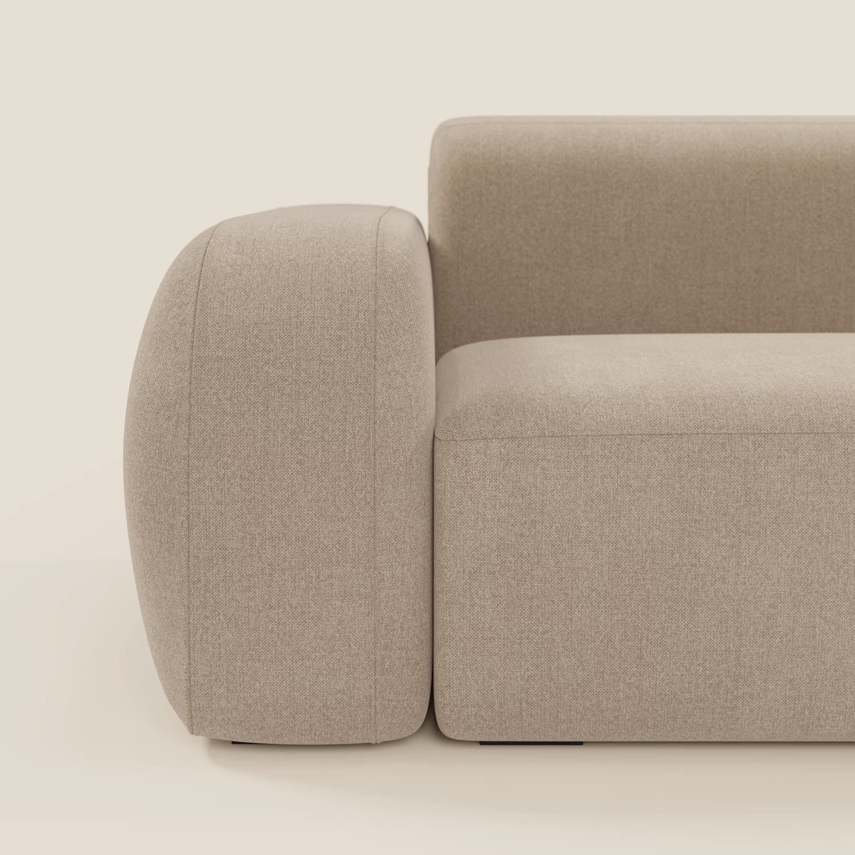 Un primo piano del divano angolare componibile e modulare BonBon di Divani.Store in tessuto smacchiabile T23 beige mostra la sua forma squadrata, l'ampia seduta e lo spesso bracciolo arrotondato, sottolineandone le linee pulite e lo stile minimalista.