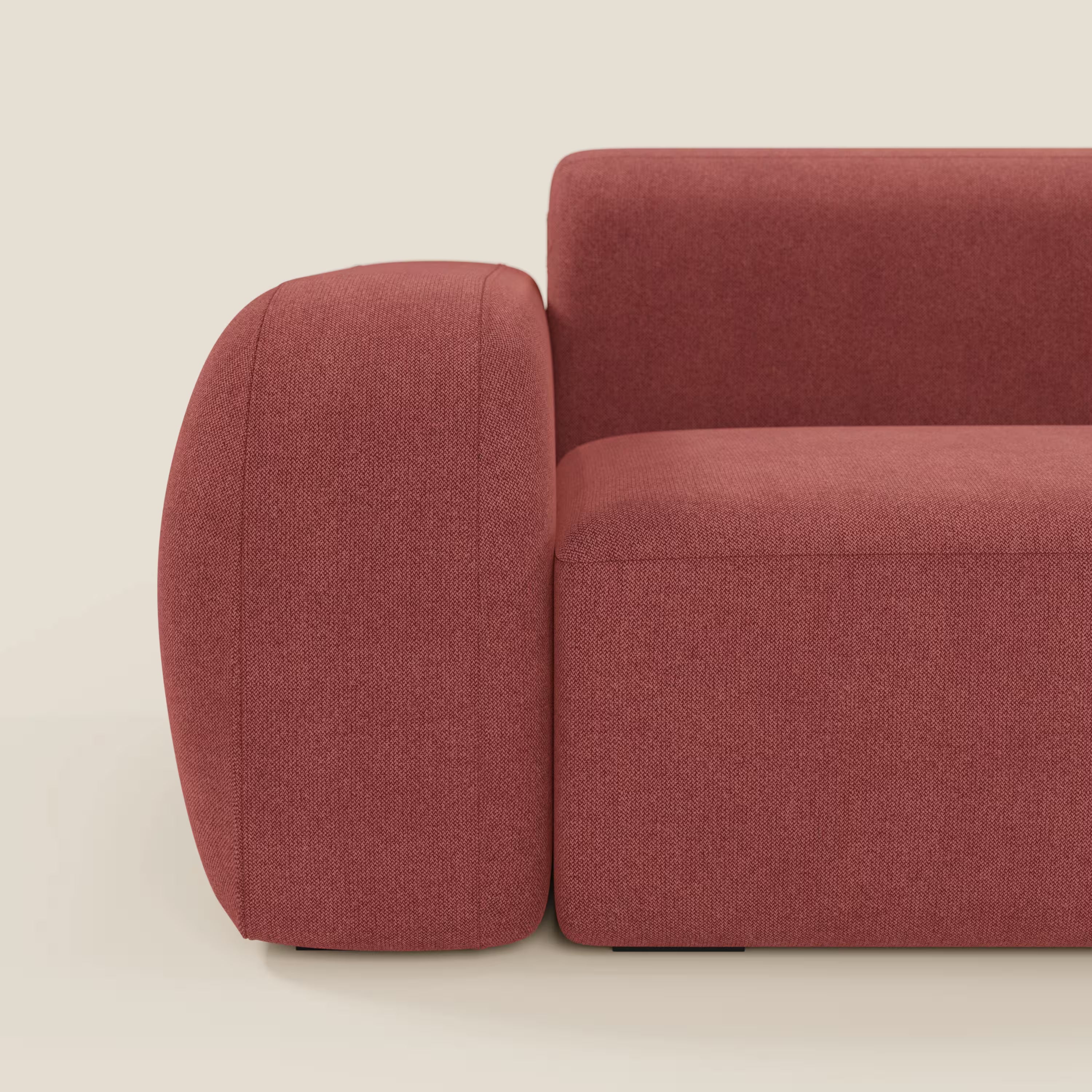 Vista laterale ravvicinata del divano angolare componibile e modulare BonBon di Divani.Store in tessuto smacchiabile T23 rosso ciliegia, caratterizzato da un moderno design a blocchi con braccioli arrotondati e linee pulite, su uno sfondo beige chiaro. Prodotto in Italia.
