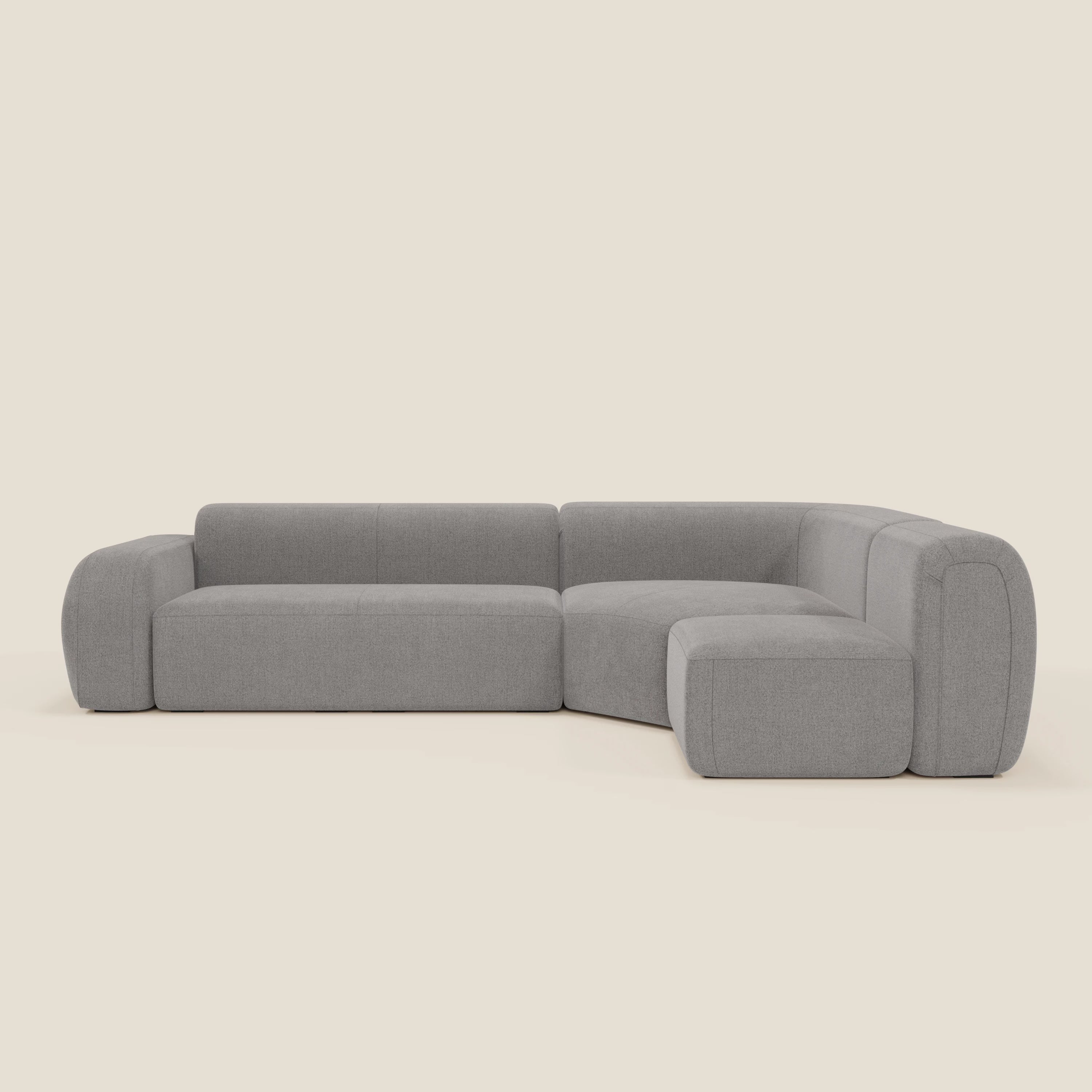Il divano angolare componibile e modulare BonBon di Divani.Store, rivestito in tessuto antimacchia T23 grigio, è caratterizzato da sedute basse e larghe e braccioli curvi. Questo moderno divano componibile italiano spicca su un semplice sfondo bianco sporco.
