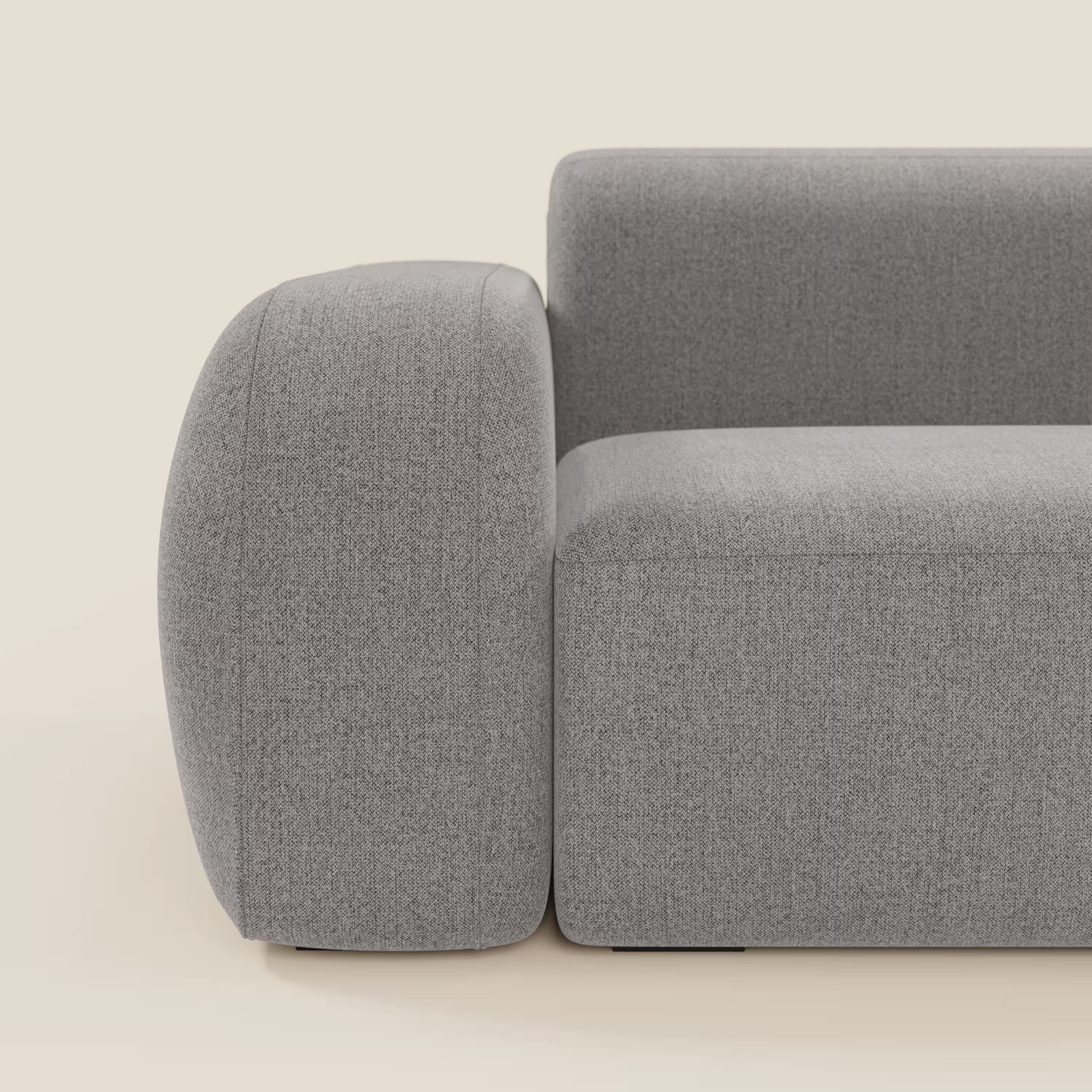 Il divano angolare componibile e modulare BonBon di Divani.Store in smacchiabile T23 grigio è caratterizzato da braccioli e schienale spessi e arrotondati, da un tessuto liscio e strutturato e da un design minimalista con linee morbide. Vista laterale su sfondo beige chiaro.