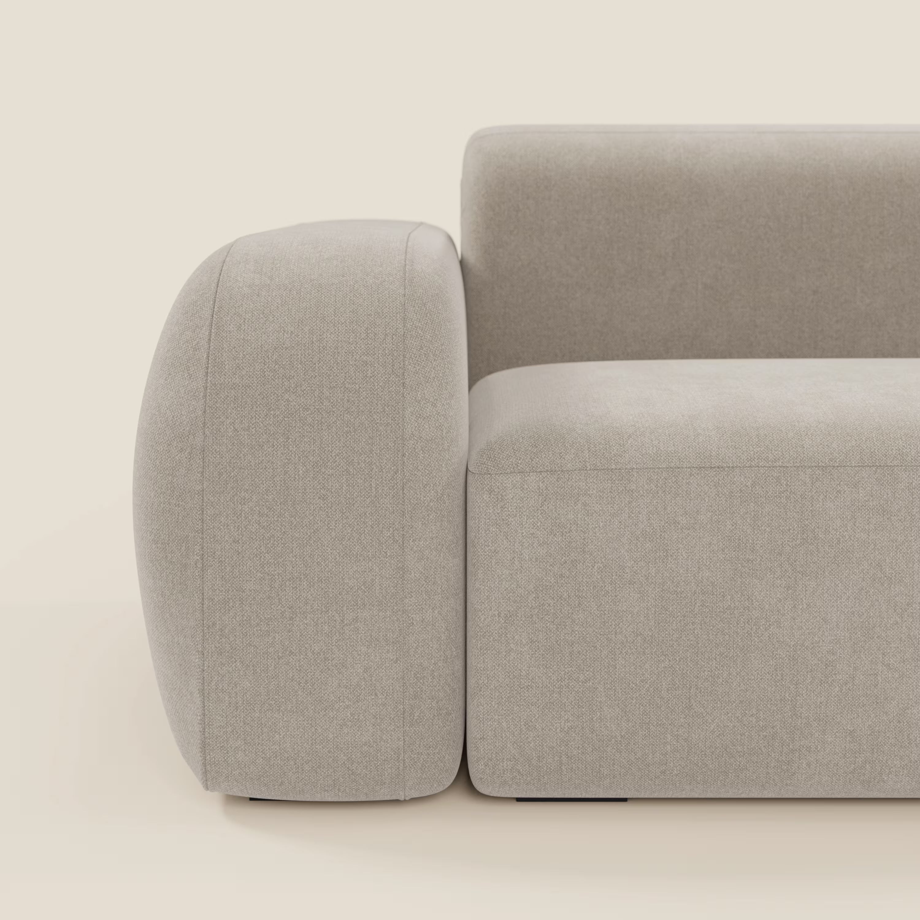 Vista laterale ravvicinata del divano BonBon angolare componibile e modulare in tessuto smacchiabile T23 panna di Divani.Store, caratterizzato da braccioli spessi e arrotondati e da una forma squadrata e moderna su uno sfondo bianco sporco. Solo una parte del divano è visibile.