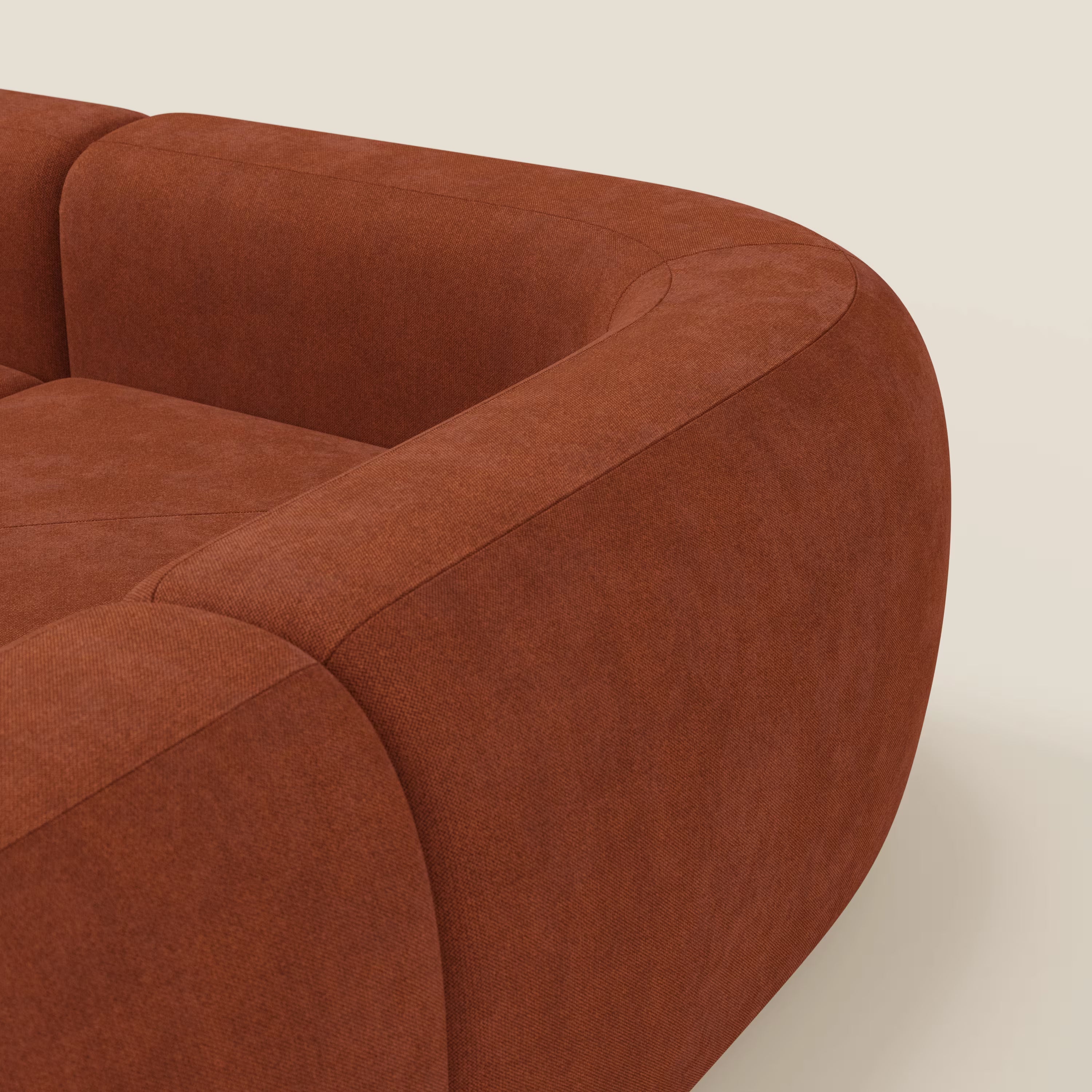 Primo piano del divano angolare componibile e modulare BonBon di Divani.Store, caratterizzato da bordi arrotondati e braccioli in tessuto ruggine T23 antimacchia. Lo sfondo bianco sporco mette in risalto la sua elegante silhouette curva.