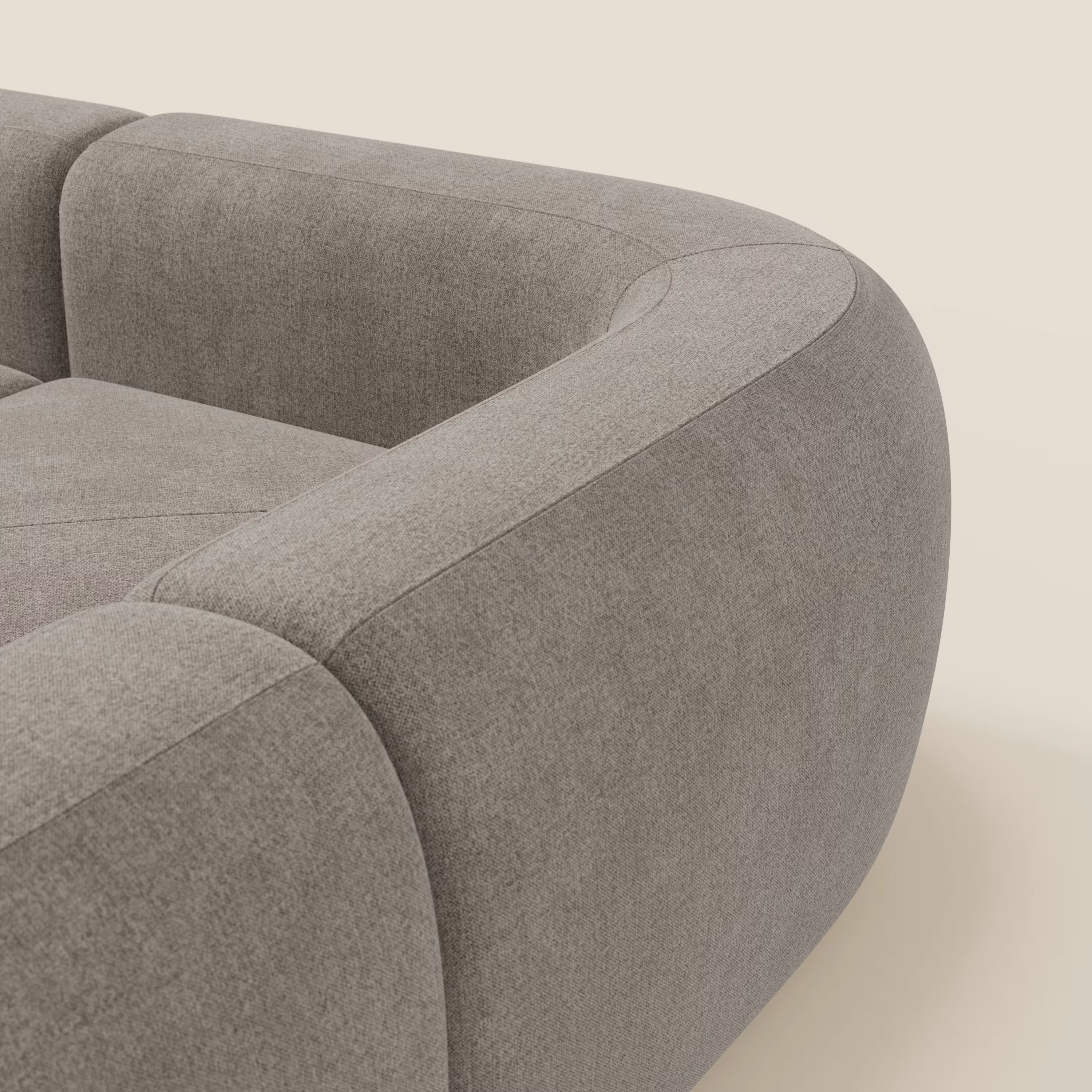 Un primo piano del divano angolare componibile e modulare BonBon di Divani.Store in tessuto smacchiabile T23 talpa mostra i bordi arrotondati, i braccioli imbottiti e le cuciture senza cuciture per un look accogliente e minimalista su uno sfondo neutro.