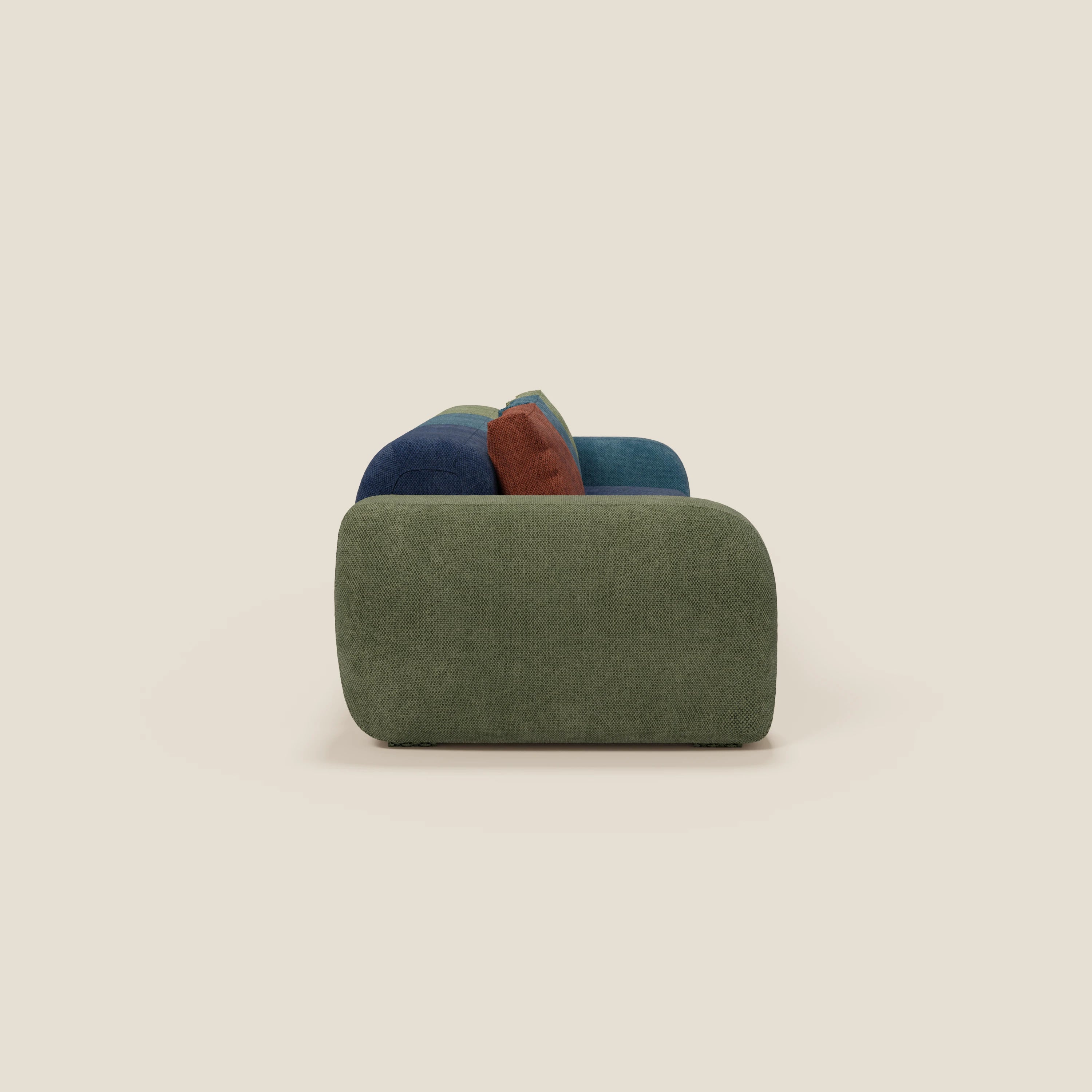 Vista laterale del divano componibile BonBon 3 sedute - edizione Grande Fratello di Divani.Store, caratterizzato da linee arrotondate, imbottitura verde oliva e tre cuscini in peluche blu, turchese e marrone su uno sfondo beige chiaro. Prodotto in Italia.