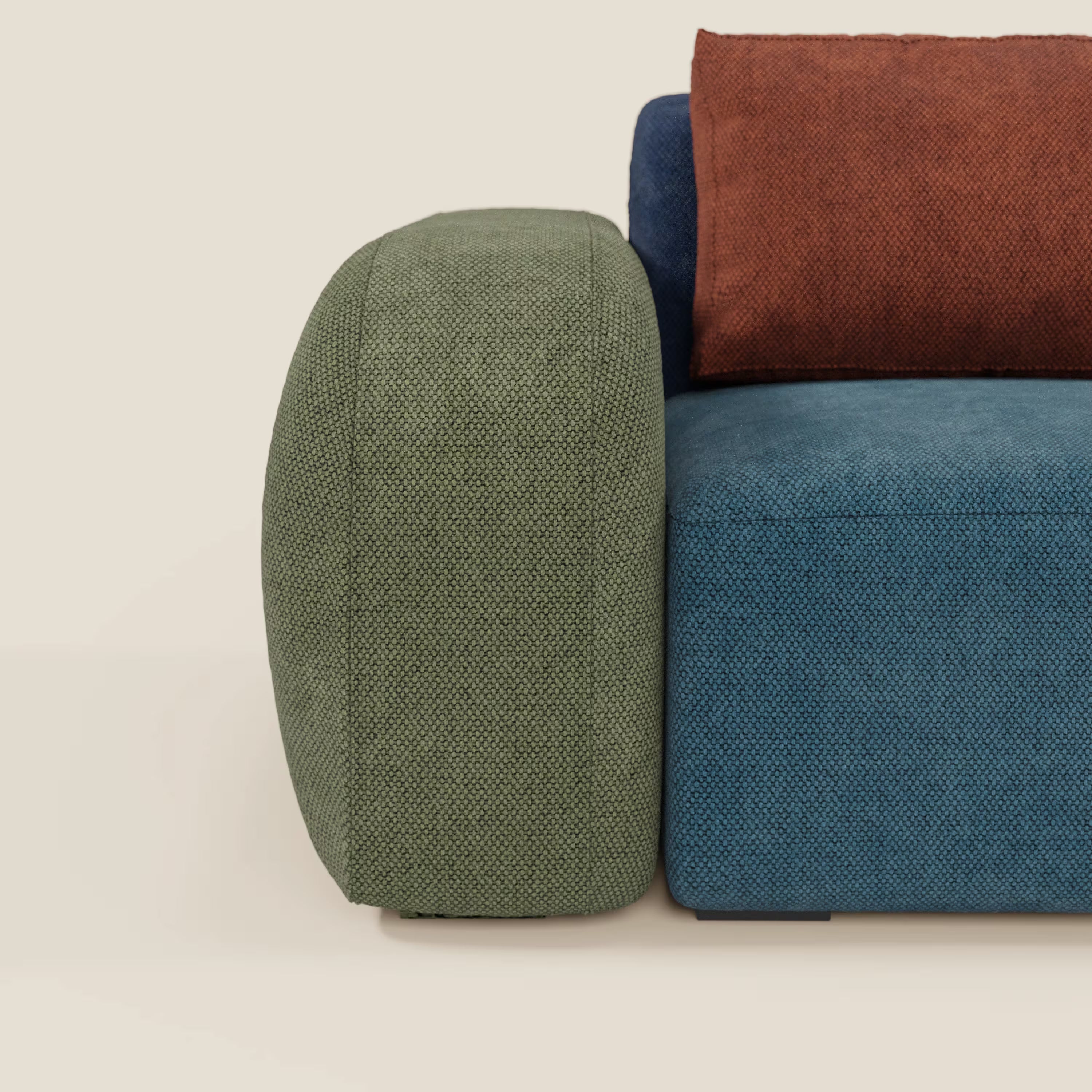 Il divano componibile BonBon 3 sedute - edizione Grande Fratello di Divani.Store è caratterizzato da un bracciolo con texture verde, una seduta in tessuto blu e un cuscino marrone rossiccio, con un design arrotondato e in tinta su uno sfondo beige chiaro. Prodotto in Italia.