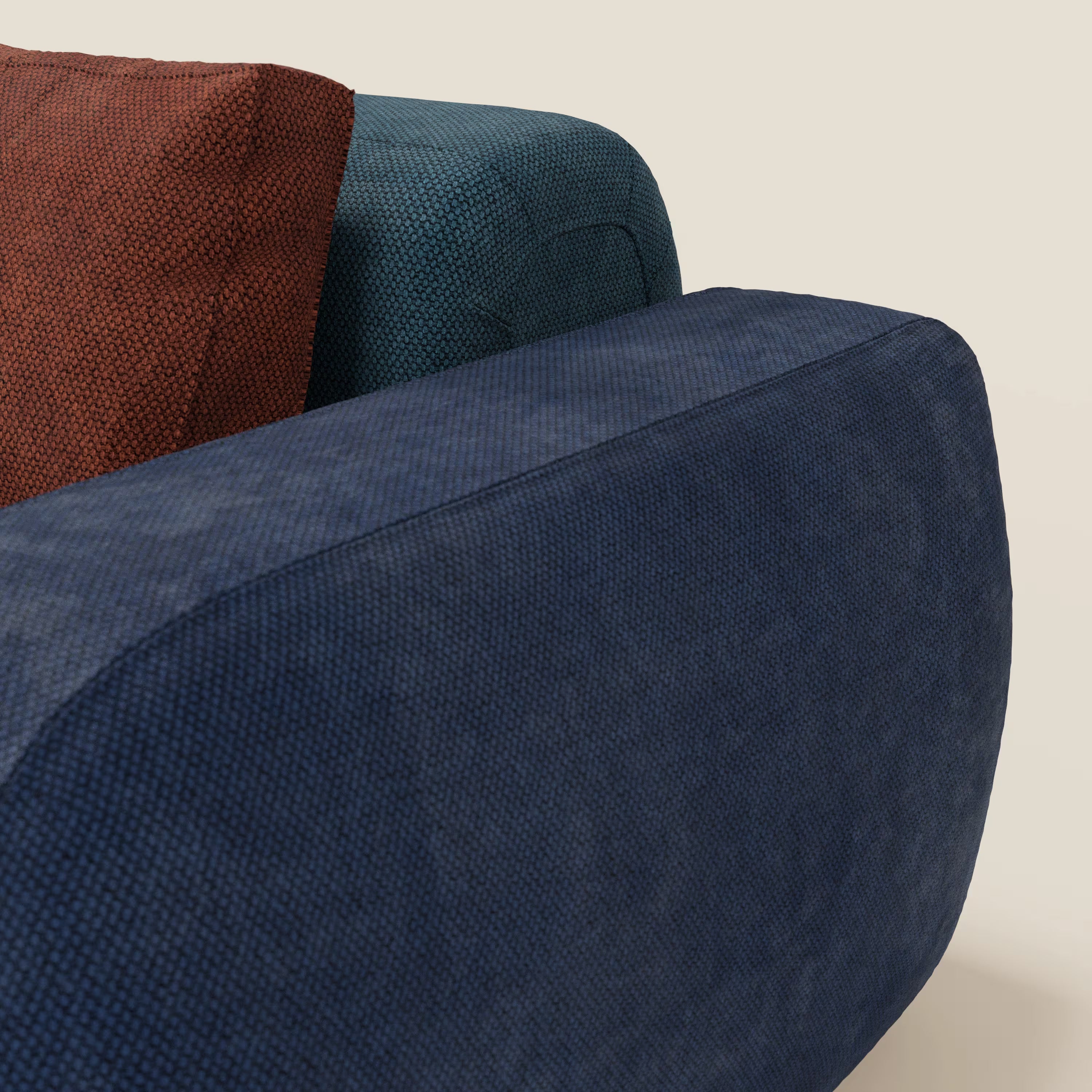 Un primo piano del divano componibile BonBon 4 posti - edizione Grande Fratello di Divani.Store è caratterizzato da tre cuscini strutturati nei colori blu scuro, verde acqua e marrone rossiccio, su uno sfondo bianco sporco che mette in risalto il suo audace design italiano.