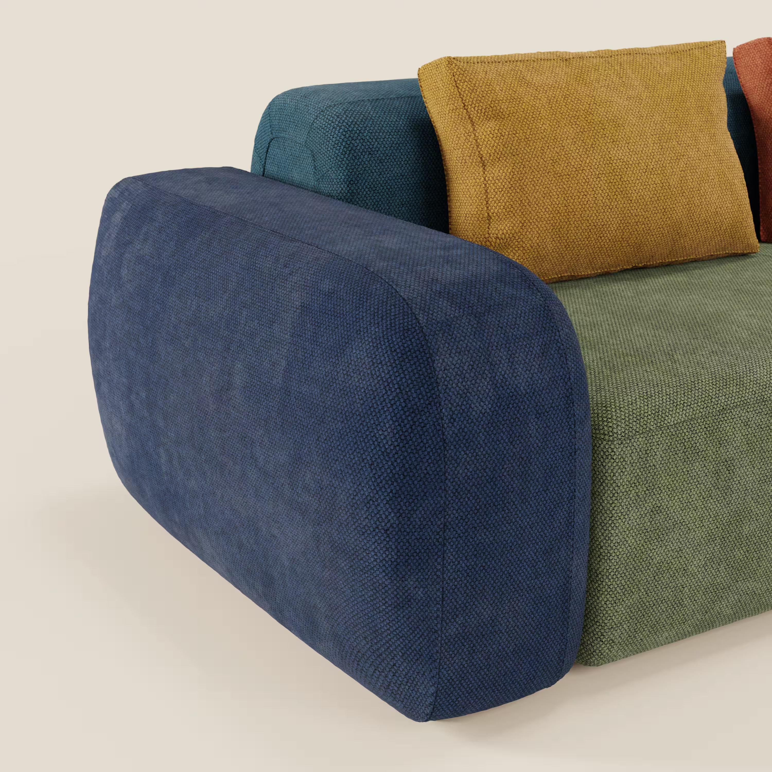 Il divano componibile angolare BonBon - Grande Fratello Edition di Divani.Store è caratterizzato da un design moderno con bracciolo arrotondato di colore blu intenso, cuscino di seduta verde, schienale blu e due cuscini di stoffa - giallo senape e arancio bruciato - su sfondo beige.