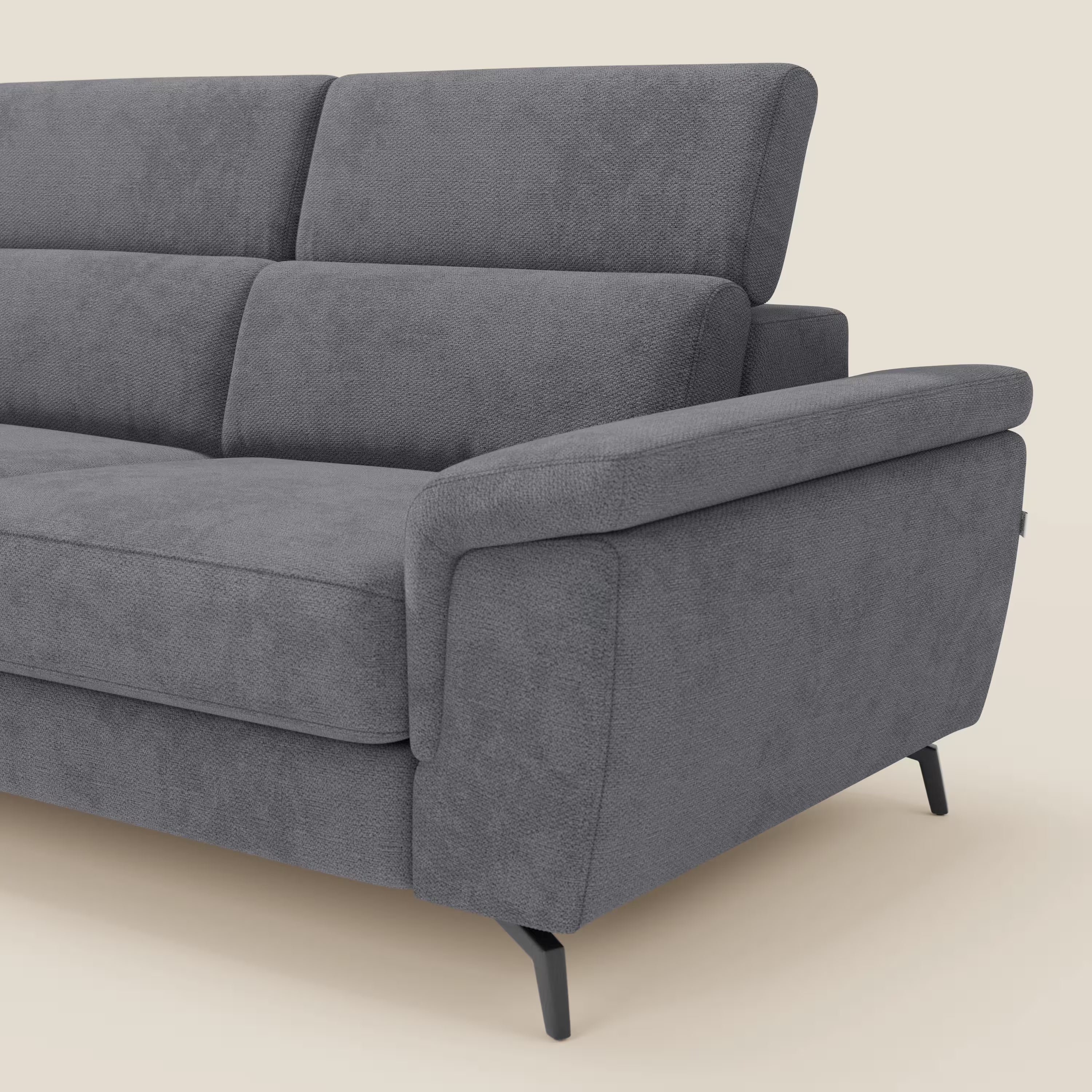 Primo piano di Estro Divano angolare estraibile di Divani.Store, caratterizzato da ampi braccioli in tessuto felpato, tre schienali imbottiti, sottili gambe in metallo nero e poggiatesta reclinabili in tessuto impermeabile grigio T14, su uno sfondo beige chiaro.