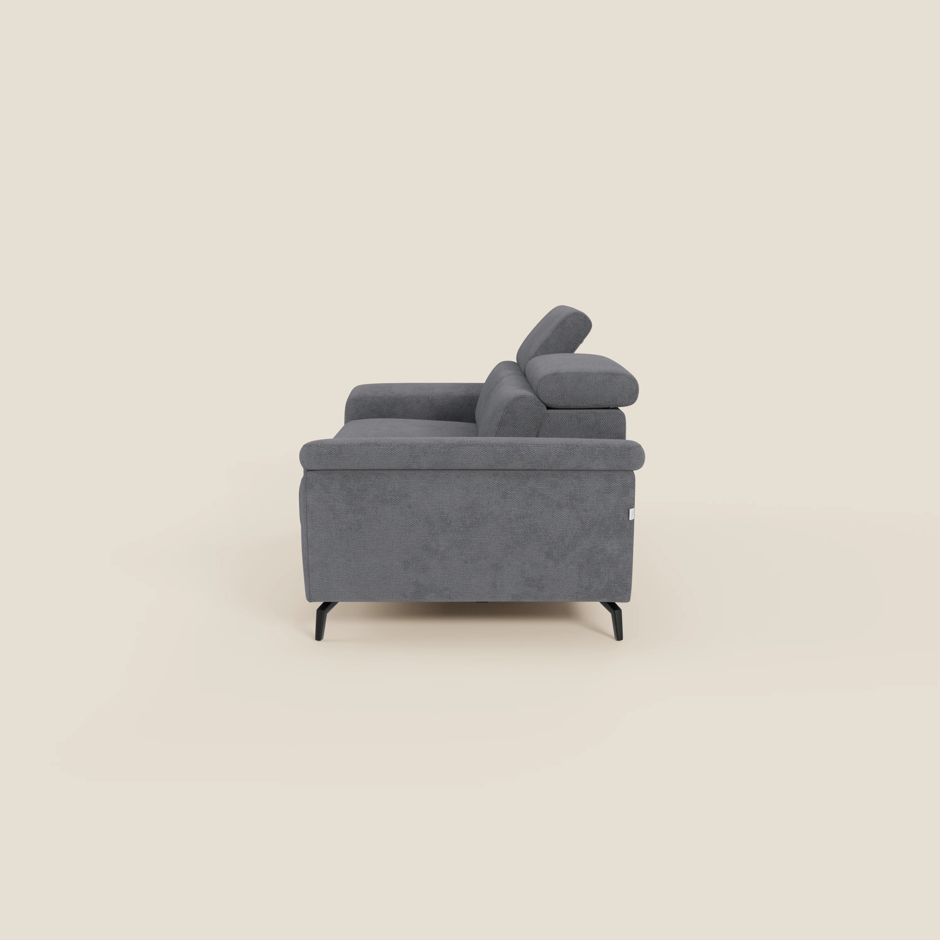 Estro Divano 3 posti con pouf estraibile di Divani.Store è presentato lateralmente in tessuto impermeabile grigio T14 con poggiatesta reclinabili, gambe sottili in metallo nero e linee pulite su sfondo beige.