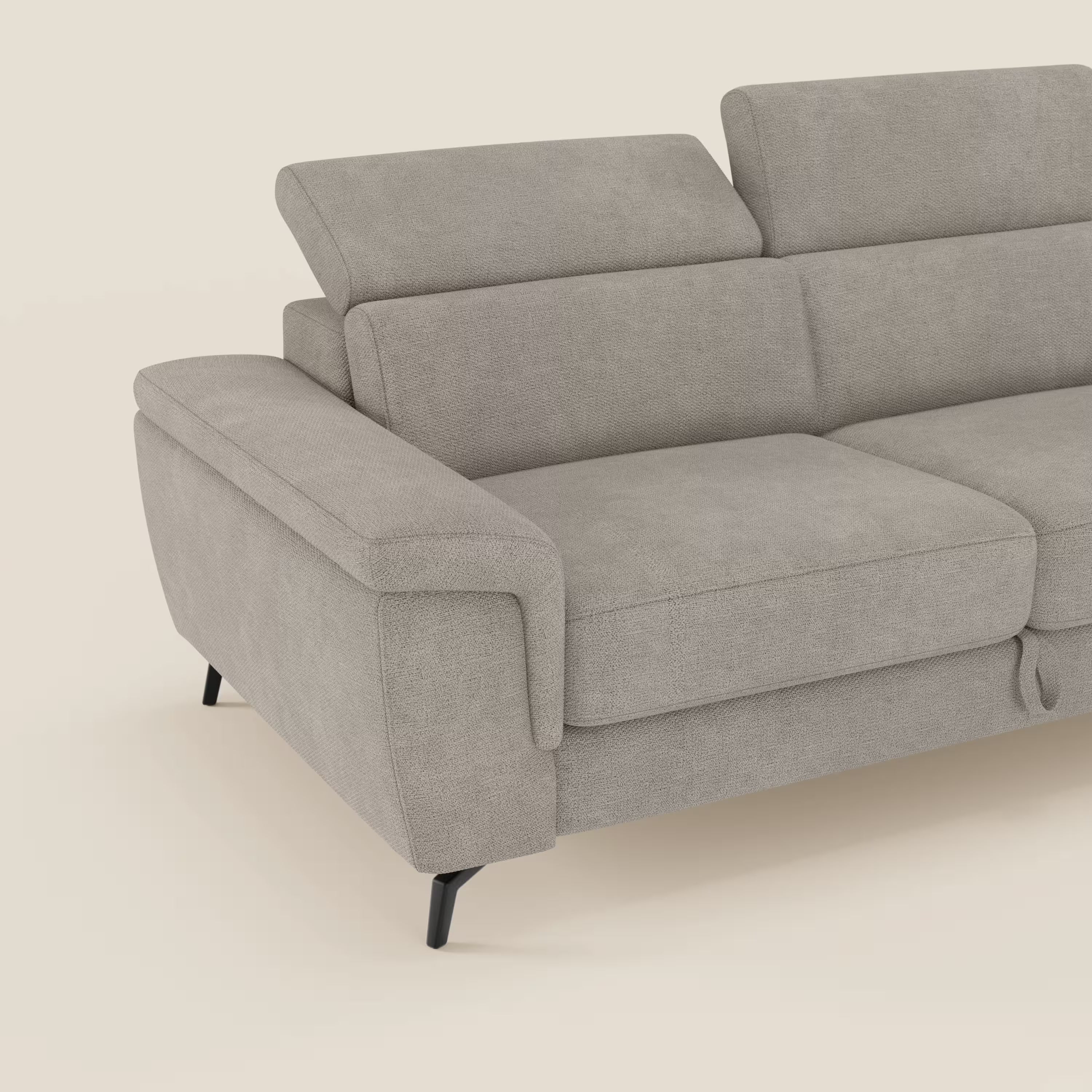 L'Estro Divano 3 posti con pouf estraibile di Divani.Store, in tessuto impermeabile T14 tortora con poggiatesta reclinabili e ampi braccioli, è mostrato parzialmente da un'angolazione frontale su sfondo bianco panna.