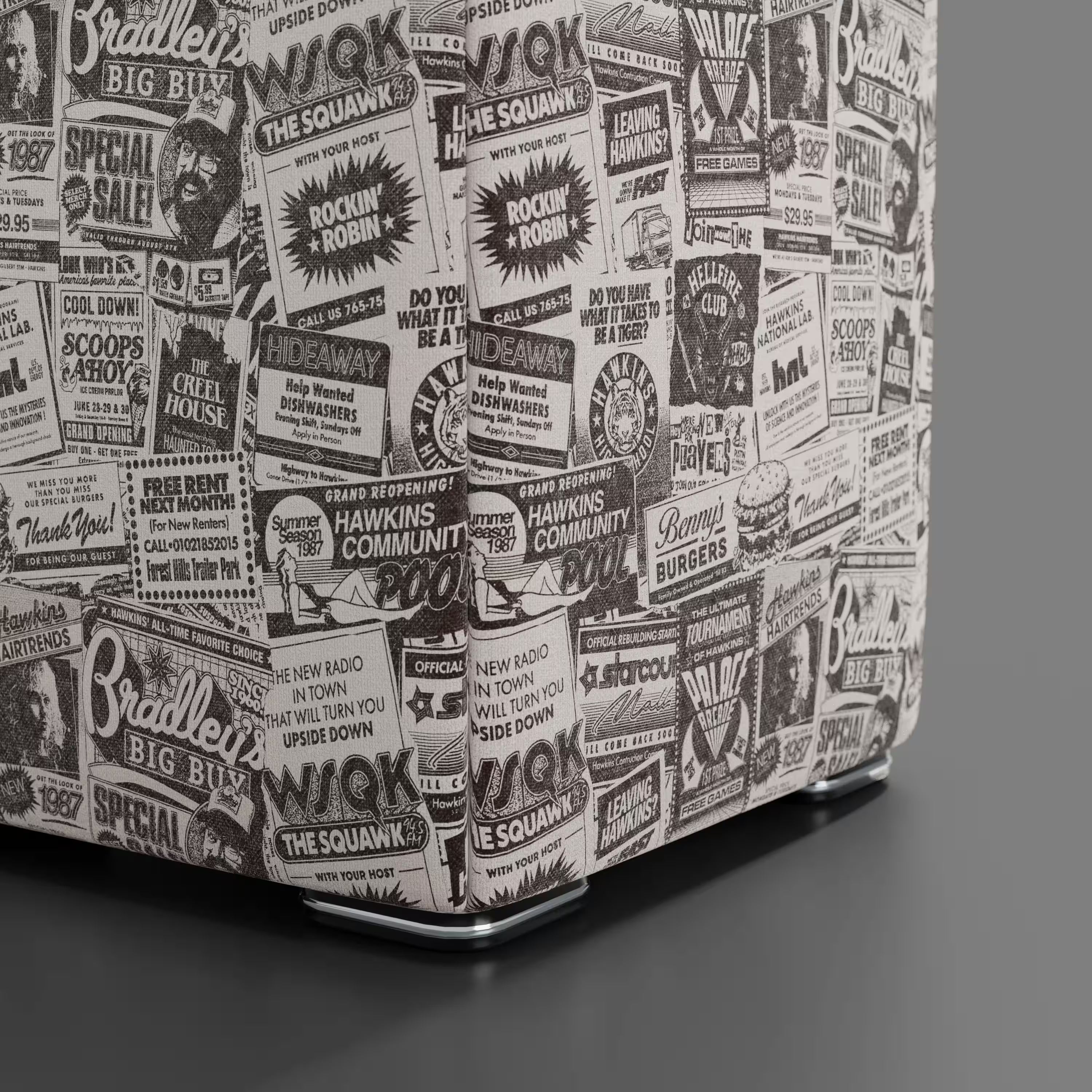 Un primo piano del Pouf Cube Hawkins Post Stranger Things - Limited Edition Netflix di Divani.Store, con stampa vintage di giornali in bianco e nero, appoggiato su un pavimento liscio grigio scuro come pezzo unico di arredamento.