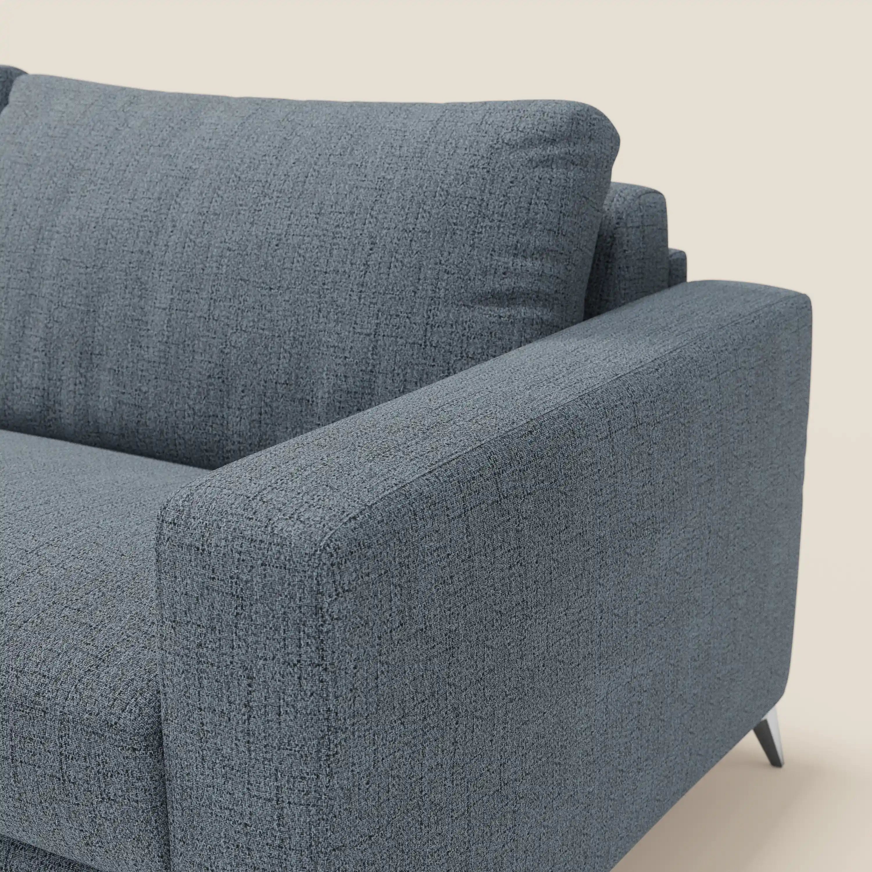 Primo piano del letto matrimoniale Alaya Divano di Divani.Store, caratterizzato da morbidi cuscini in tessuto impermeabile T03 blu. L'attenzione al bracciolo sinistro, alla seduta e al cuscino dello schienale ne evidenzia la trama e il design minimale e squadrato su uno sfondo chiaro.