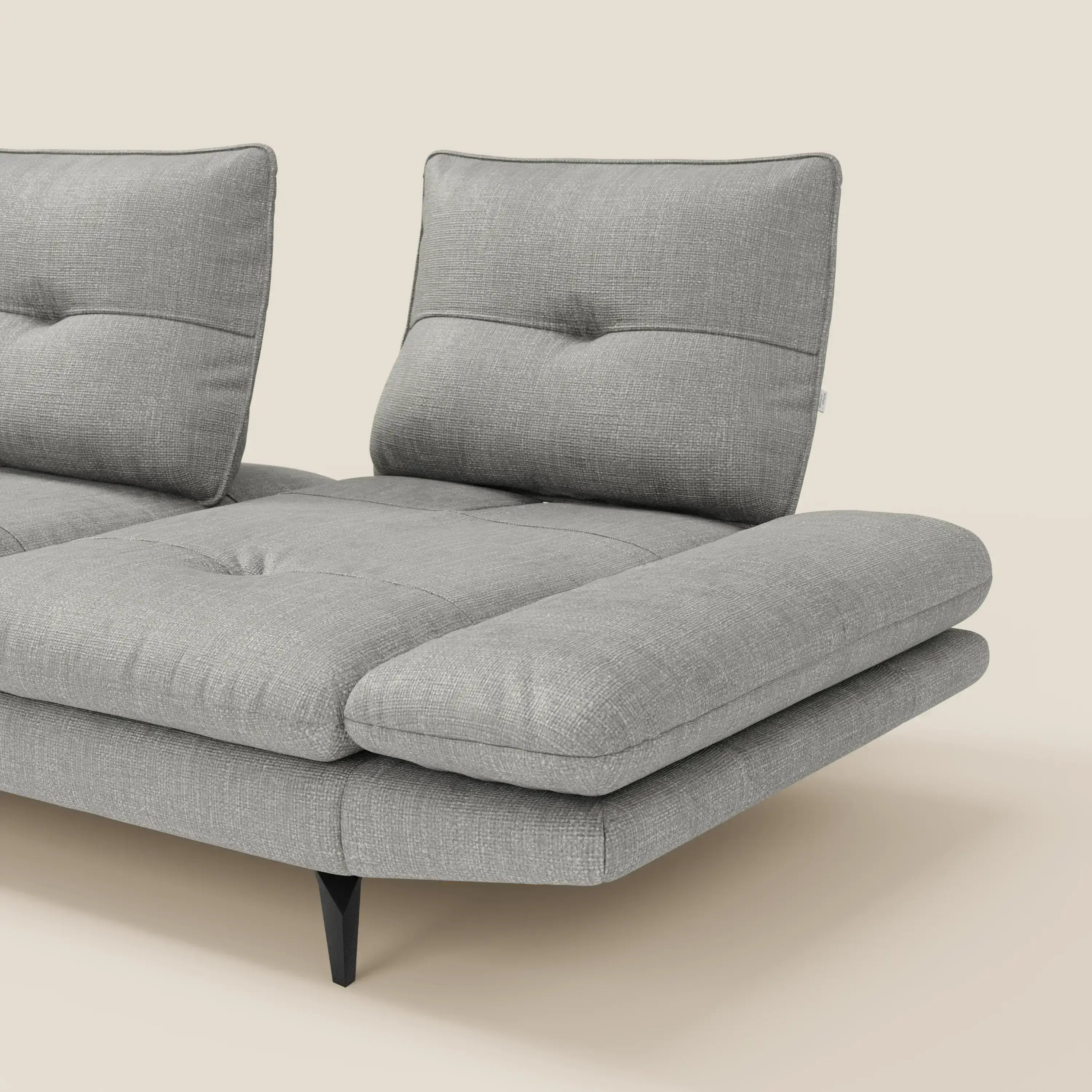 L'Ardex Divano con penisola di Divani.Store è caratterizzato da due ampie sedute, schienali con inserti in peluche, gambe angolari nere ed elegante tessuto impermeabile grigio T06 con braccioli regolabili e schienali scorrevoli, su sfondo beige.