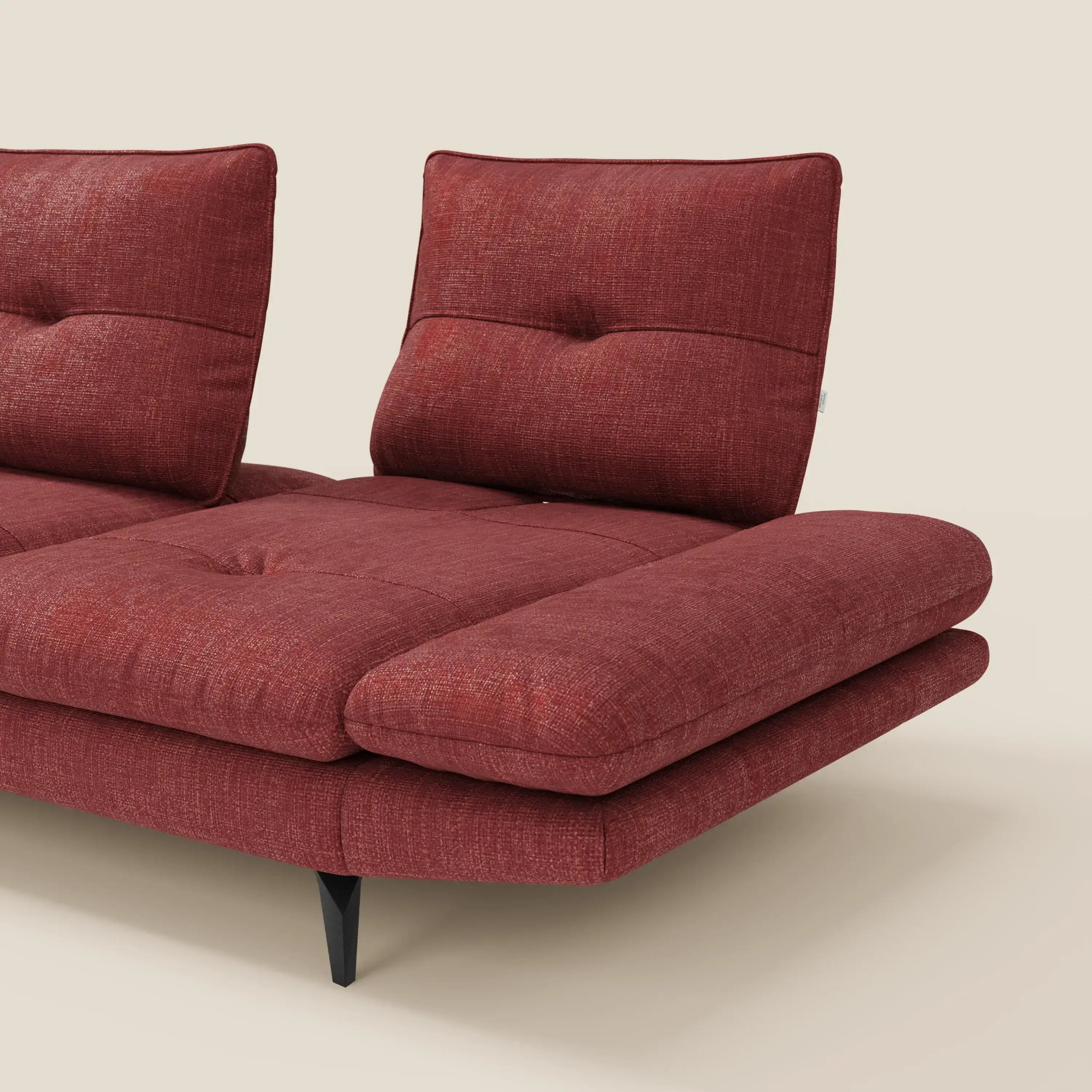 Primo piano del divano Ardex Divano con penisola di Divani.Store in elegante tessuto impermeabile rosso T06, con due schienali regolabili, cuscini trapuntati e gambe in metallo nero. Solo una parte del divano moderno è visibile su uno sfondo beige chiaro.