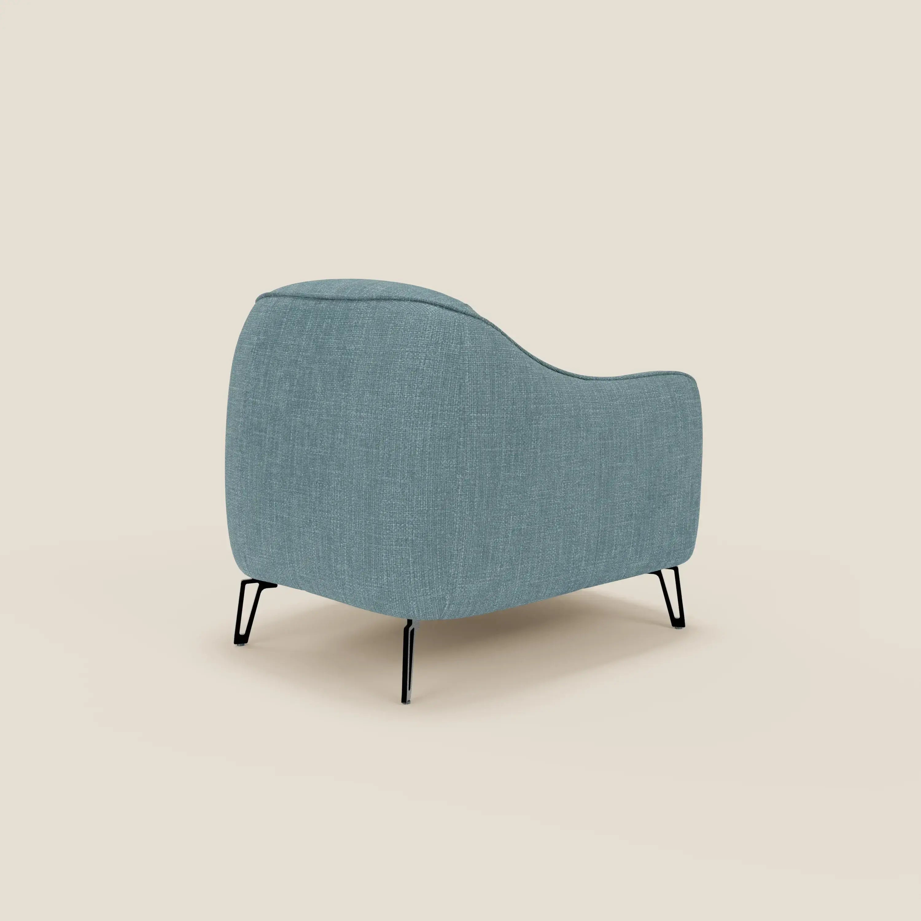 La poltroncina Avela di Divani.Store, in morbido tessuto impermeabile T06 azzurro, è caratterizzata da bordi arrotondati e gambe in metallo nero. Vista di spalle e di lato su sfondo beige, offre un comfort senza tempo e un design moderno.