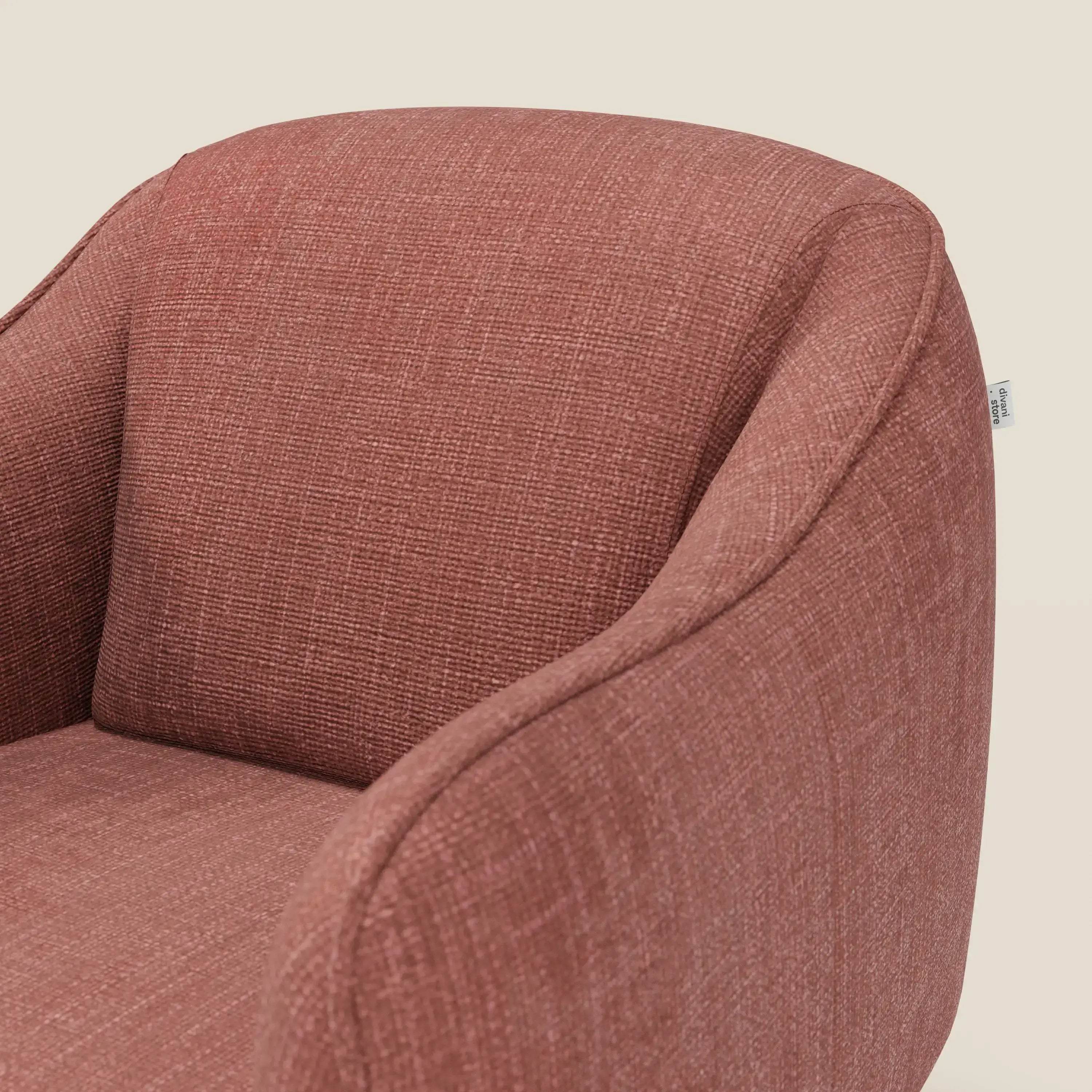 Primo piano di Avela Poltroncina di Divani.Store, una poltrona moderna in morbido tessuto impermeabile T06 corallo con schienale e braccioli curvi. Una piccola etichetta in tessuto caratterizza il lato destro. Lo sfondo è un semplice beige chiaro.