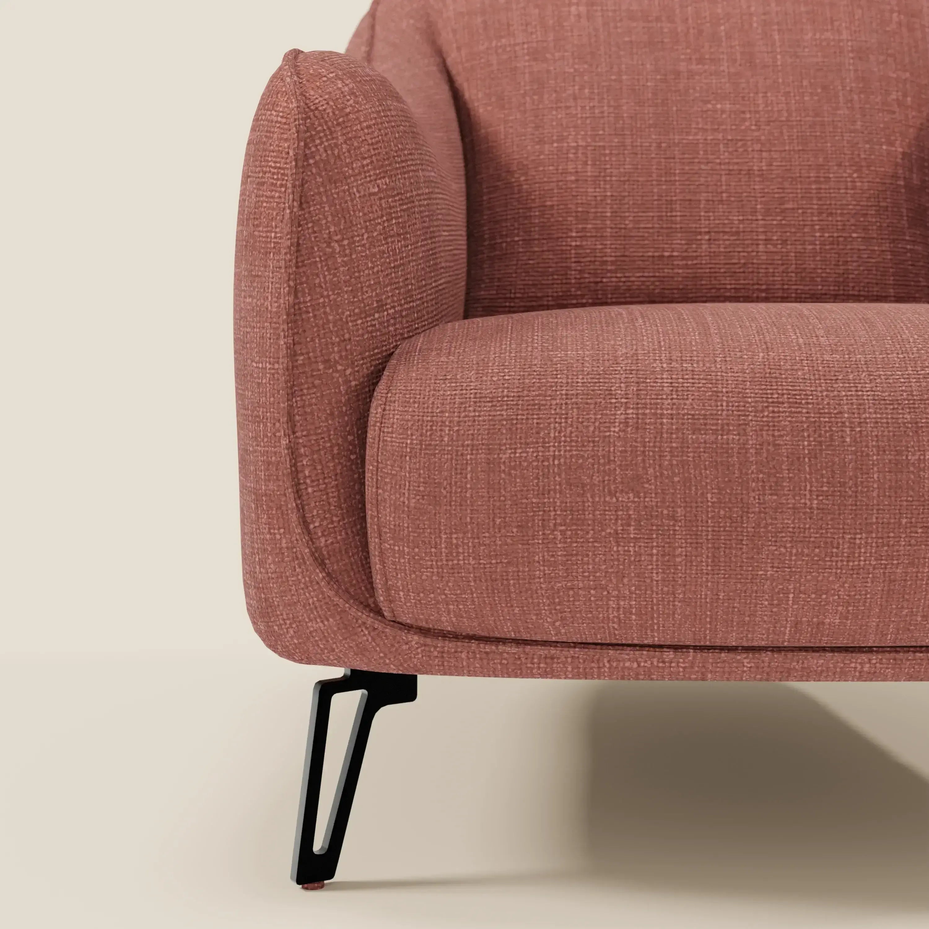Primo piano di Avela Poltroncina di Divani.Store, che mostra il bracciolo sinistro e il cuscino in morbido tessuto corallo impermeabile T06. Le eleganti gambe in metallo nero e lo sfondo beige ne evidenziano le linee pulite e il comfort moderno.