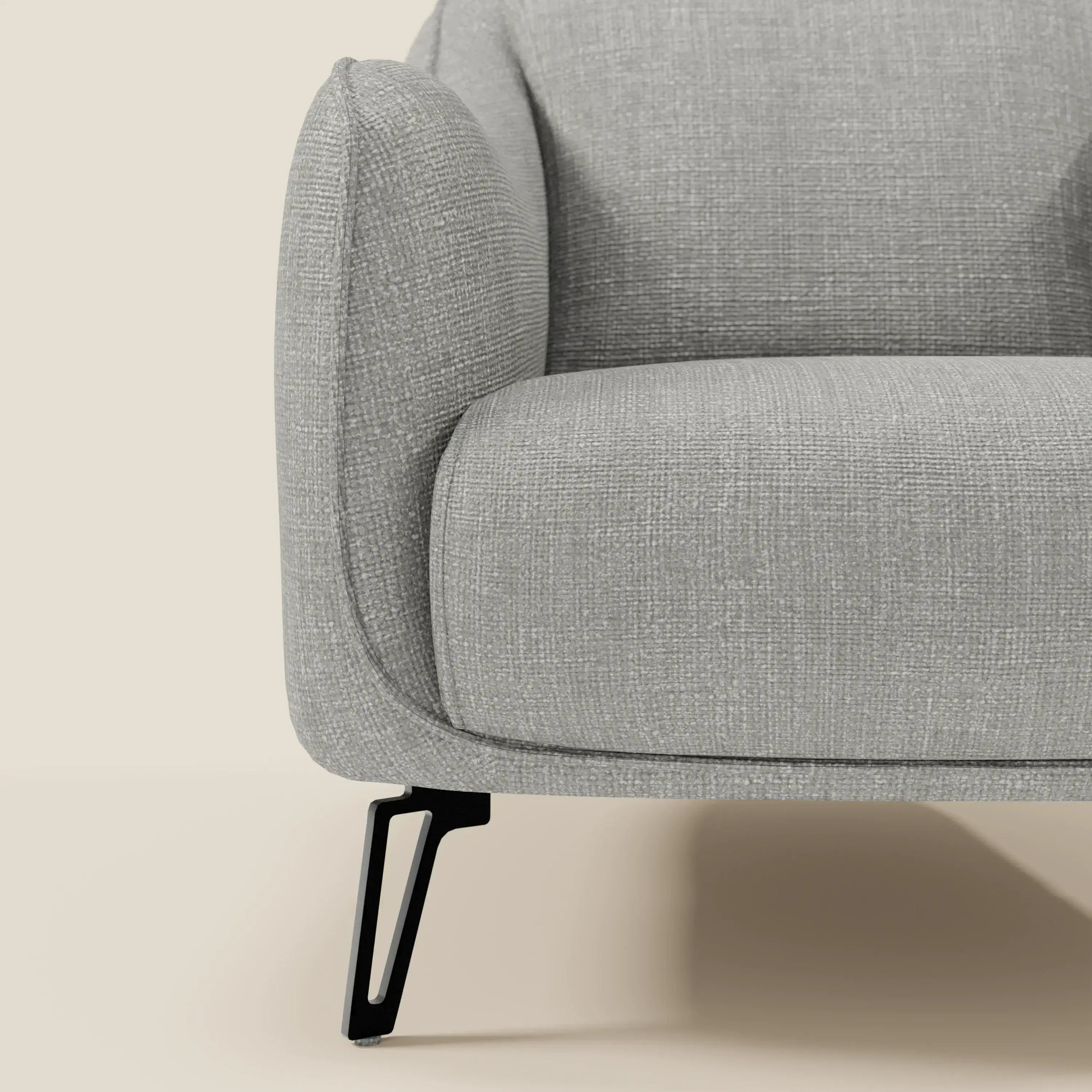 Primo piano di Avela Poltroncina di Divani.Store in morbido tessuto impermeabile grigio T06, con bracciolo moderno, cuscino di seduta ed elegante gamba in metallo nero su uno sfondo beige neutro.