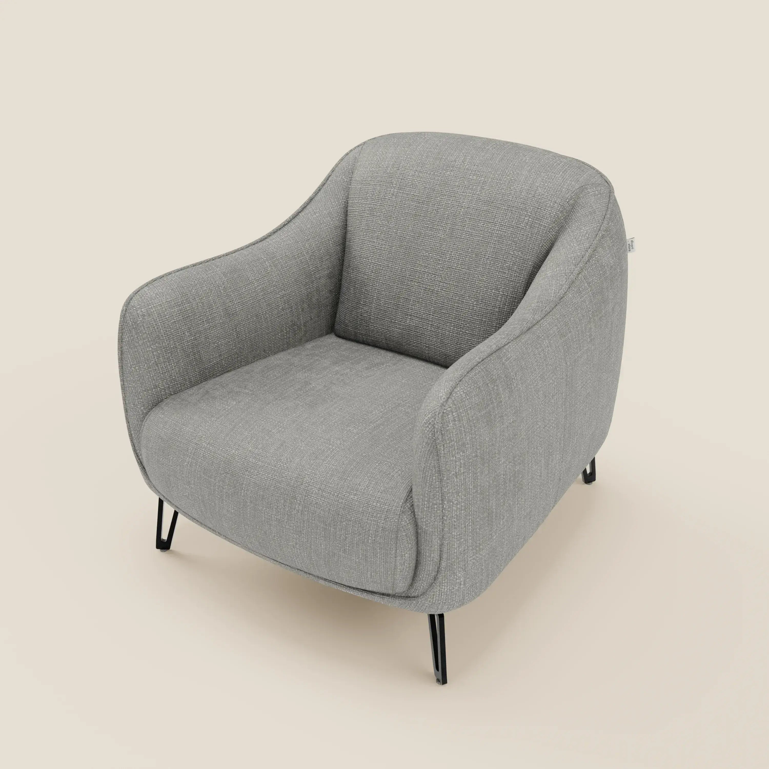 Avela Poltroncina di Divani.Store offre un comfort senza tempo grazie ai bordi morbidi e arrotondati, agli ampi braccioli imbottiti e alle gambe angolate in metallo nero rivestite in tessuto impermeabile grigio chiaro T06, su uno sfondo bianco sporco.